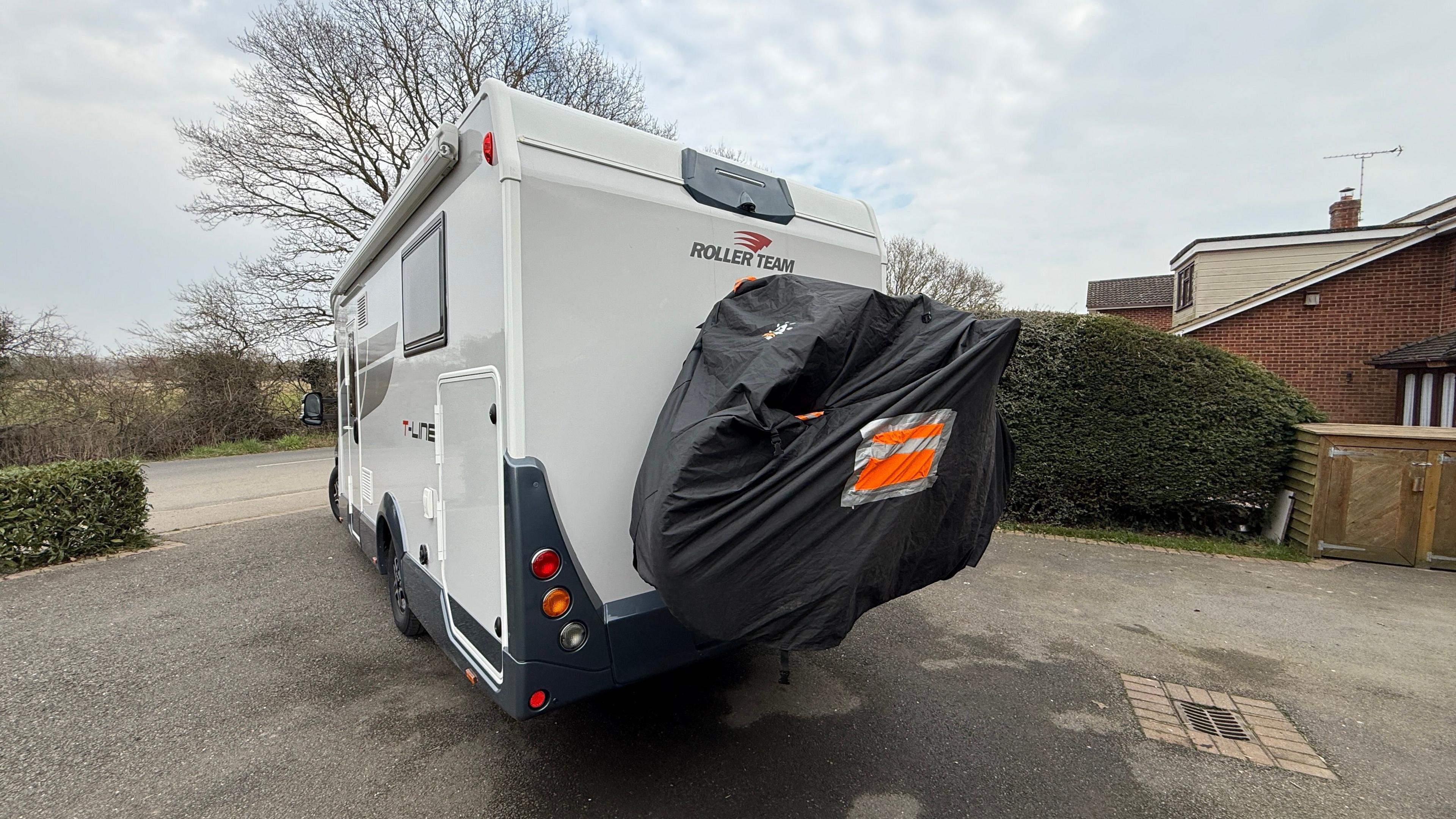 Long shot showing the back of the couple's motorhome and the bike rack, zipped inside a black cover