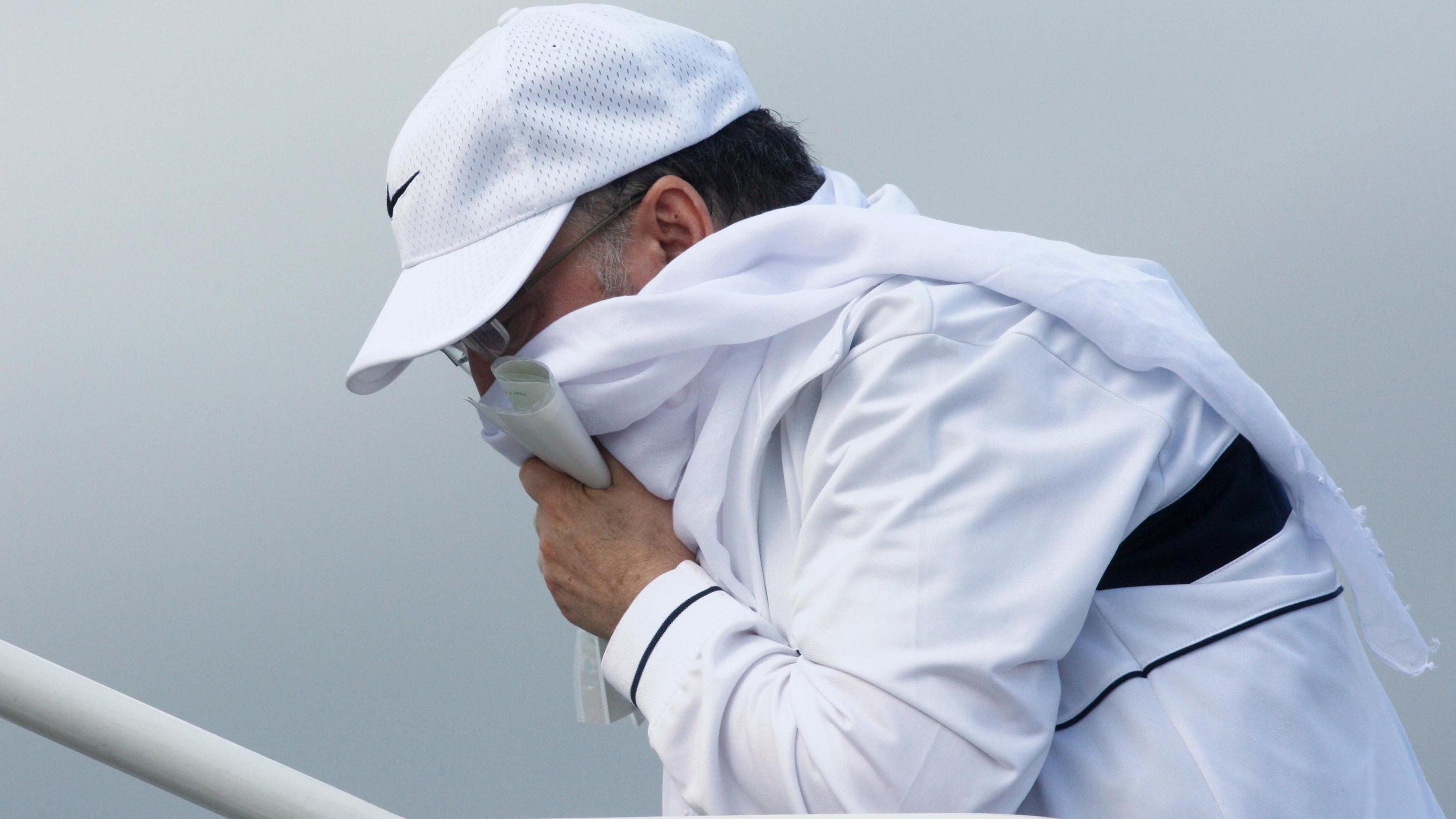 Megrahi climbing the steps of a plane at Glasgow Airport. He wearing a white tracksuit, white Nike baseball cap, and is holding a white scarf around his face.