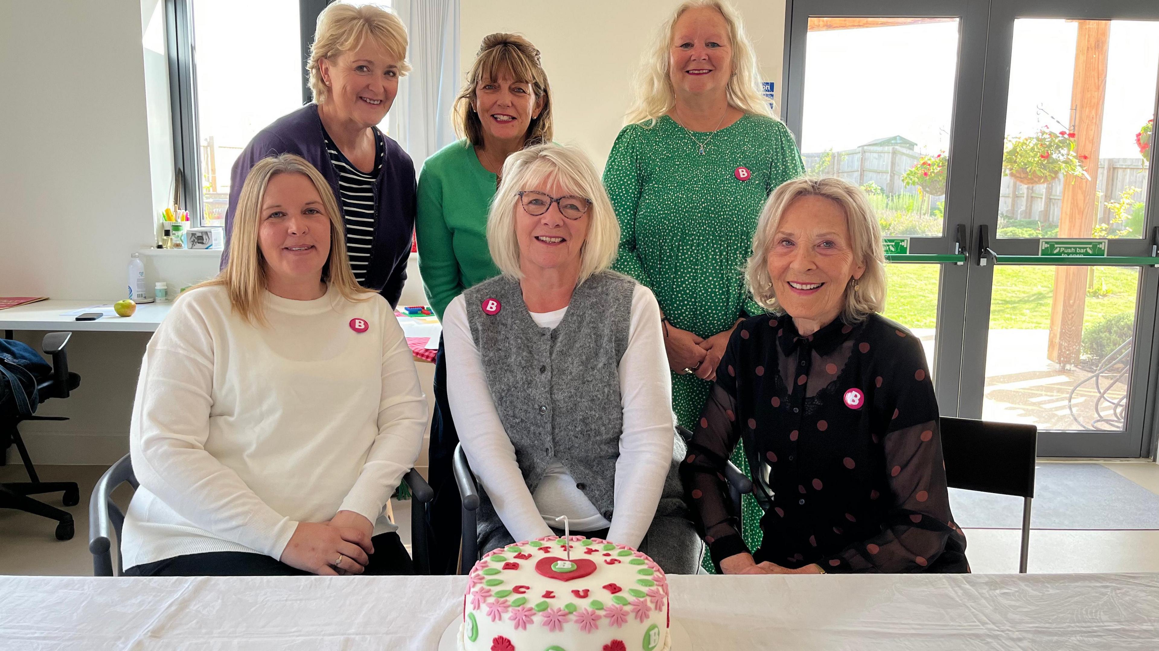 Organiser Sarah Reed sits surrounded by other women and in front of her is a beautiful cake with Betty's Club written on it in red icing. 