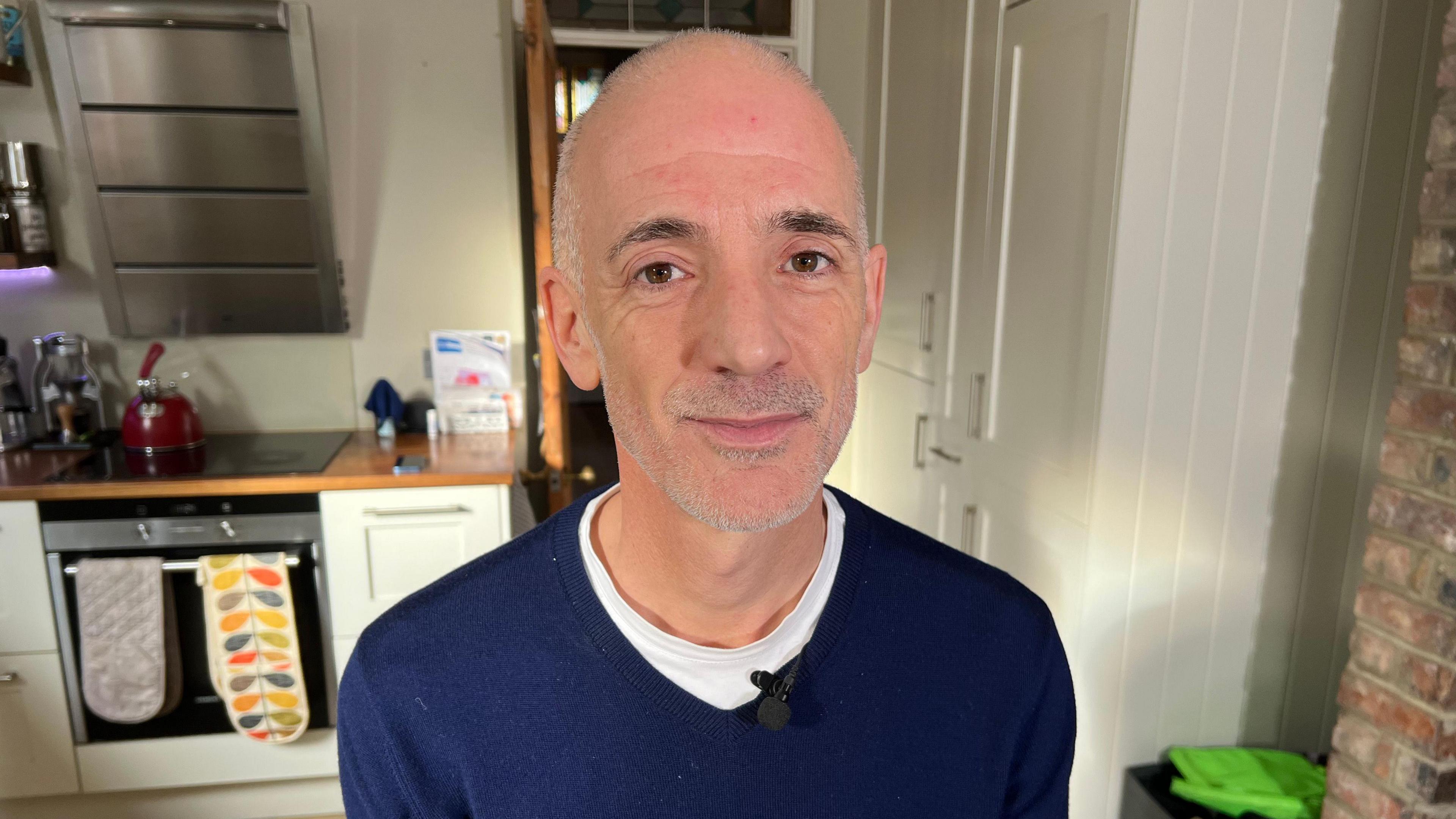 Dr Tim Williams wearing a dark top in a kitchen smiling at the camera