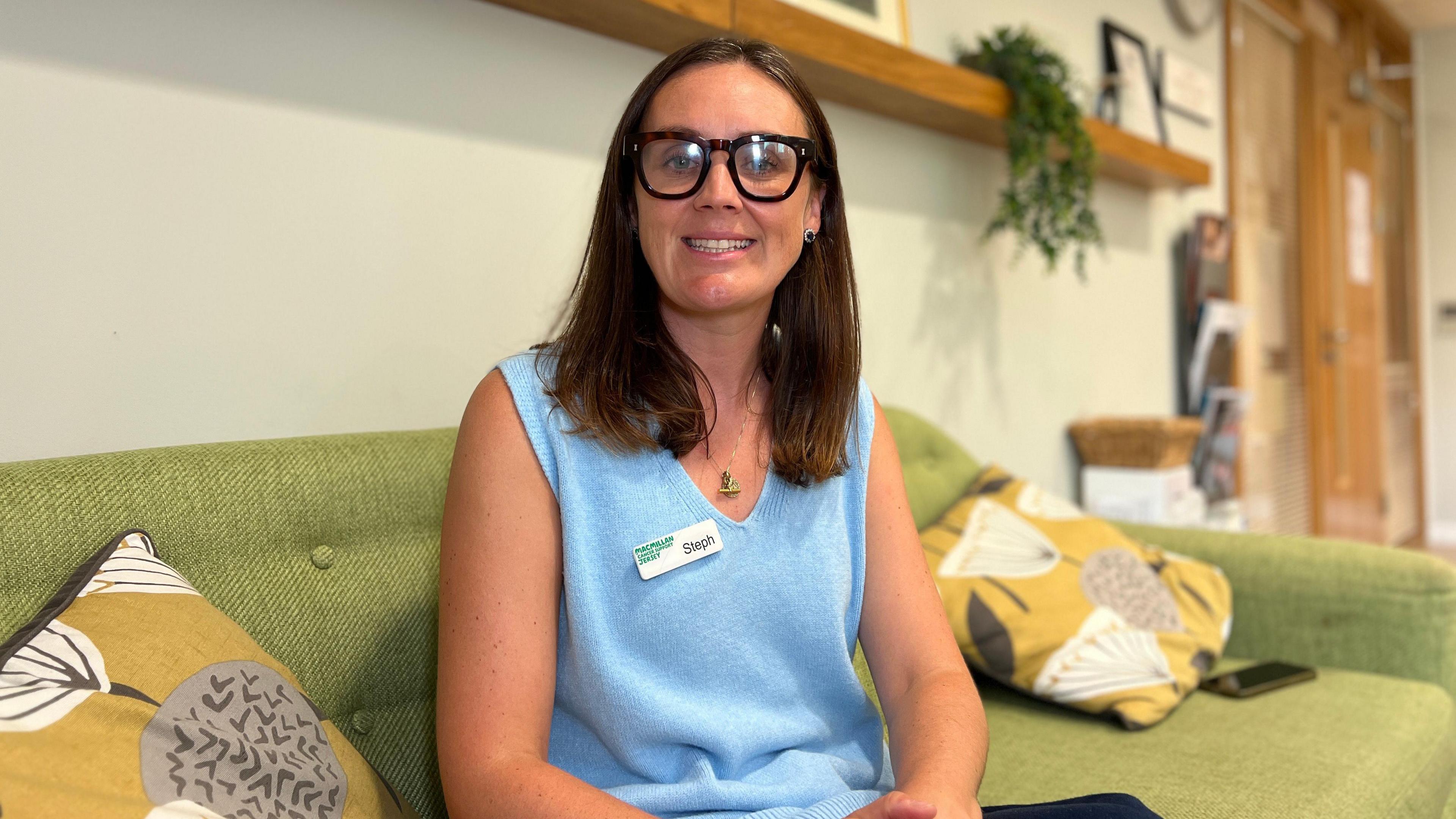 Steph smiles at the camera while sitting on a sofa at MacMillan Jersey