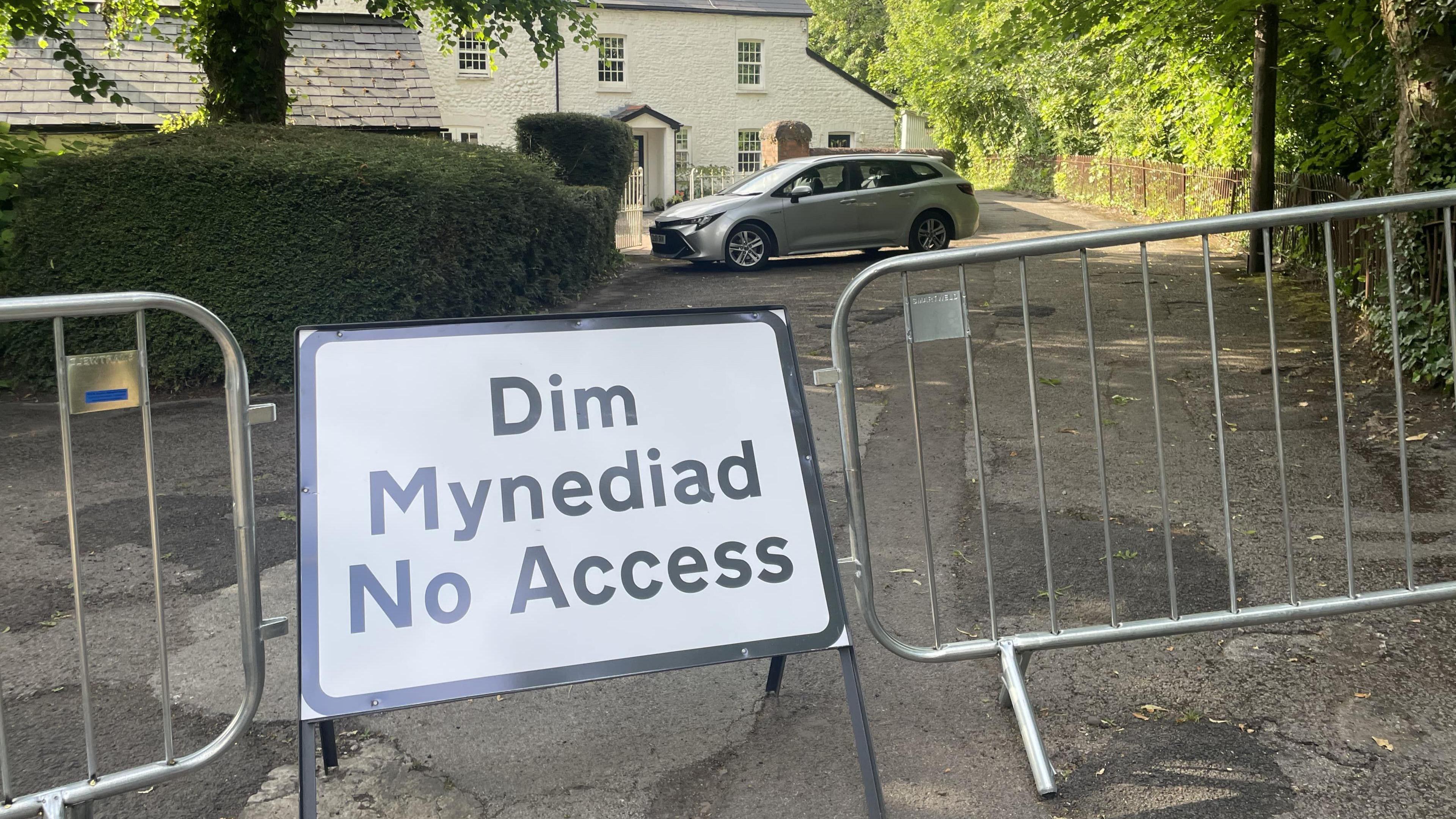A no access sign linking barriers in front of a house with a silver car parked outside.