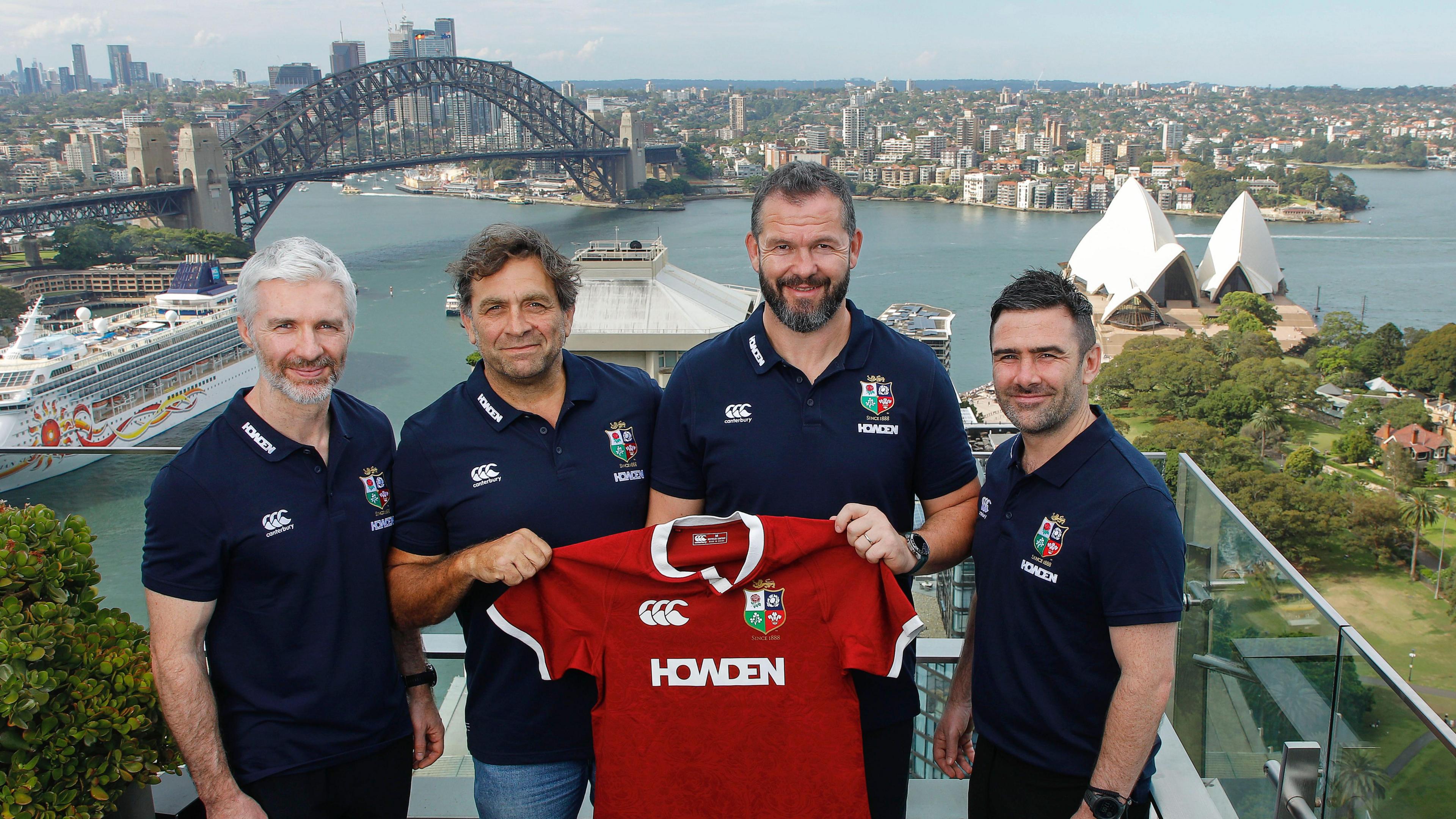 Coaches Aled Walters, David Nucifora, Andy Farrell and Vinny Hammond holding a Lions shirt in front of the Sydney skyline