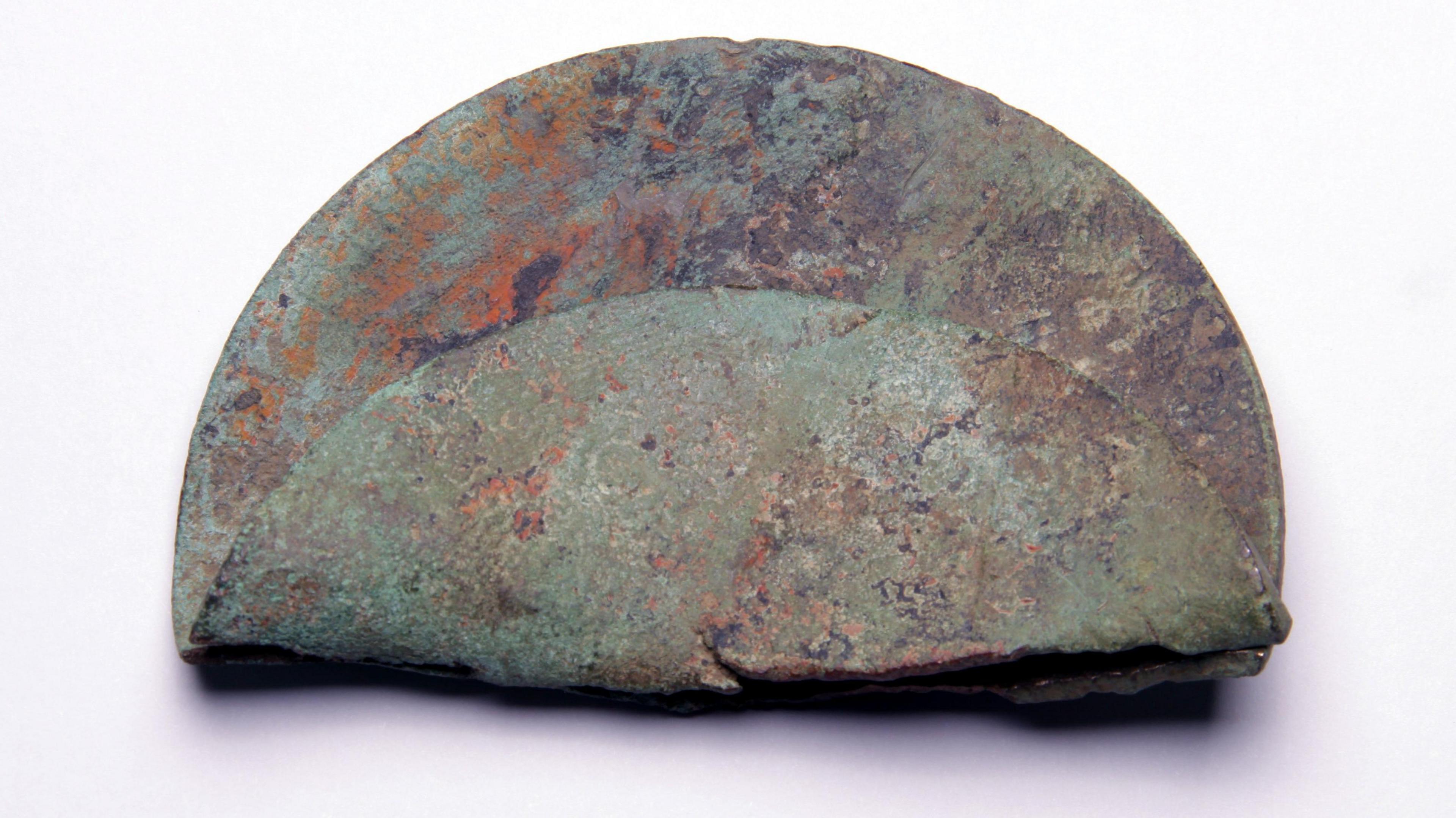 A circular metal plaque folded in half. It is circular, green and rusty