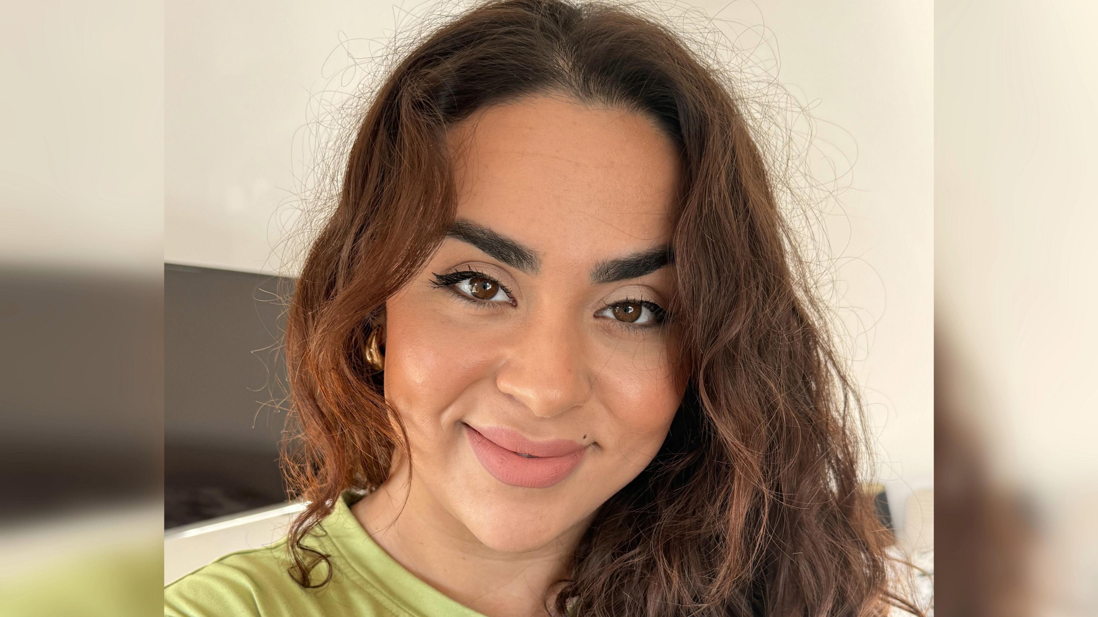 A woman with brown curly hair smiling wearing a green t-shirt. 