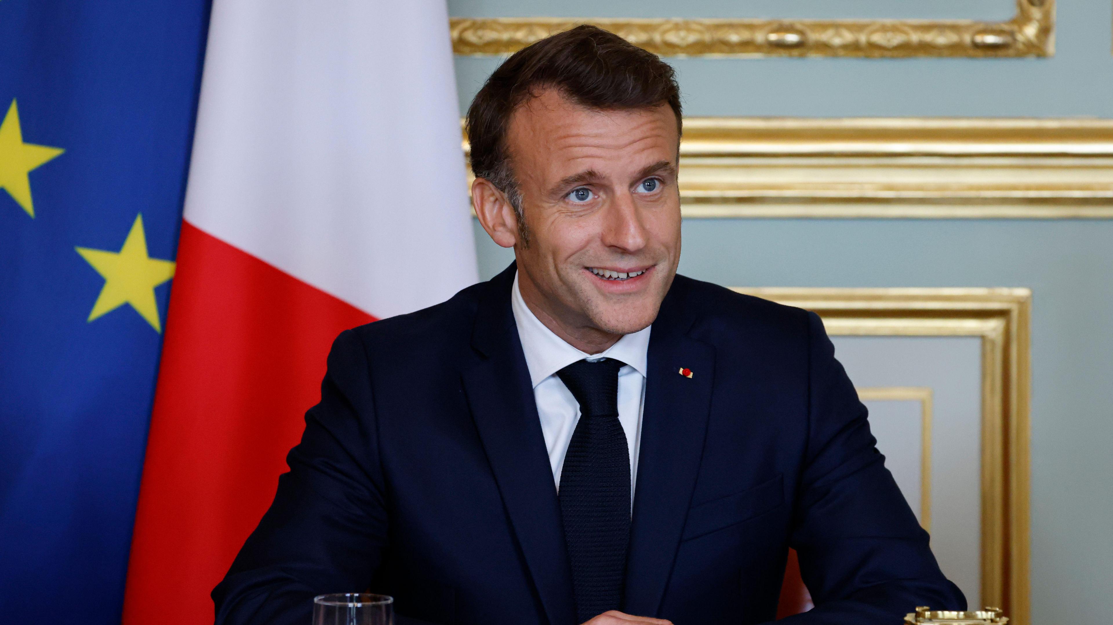 Emmanuel Macron smiles at a meeting as he sits at a table