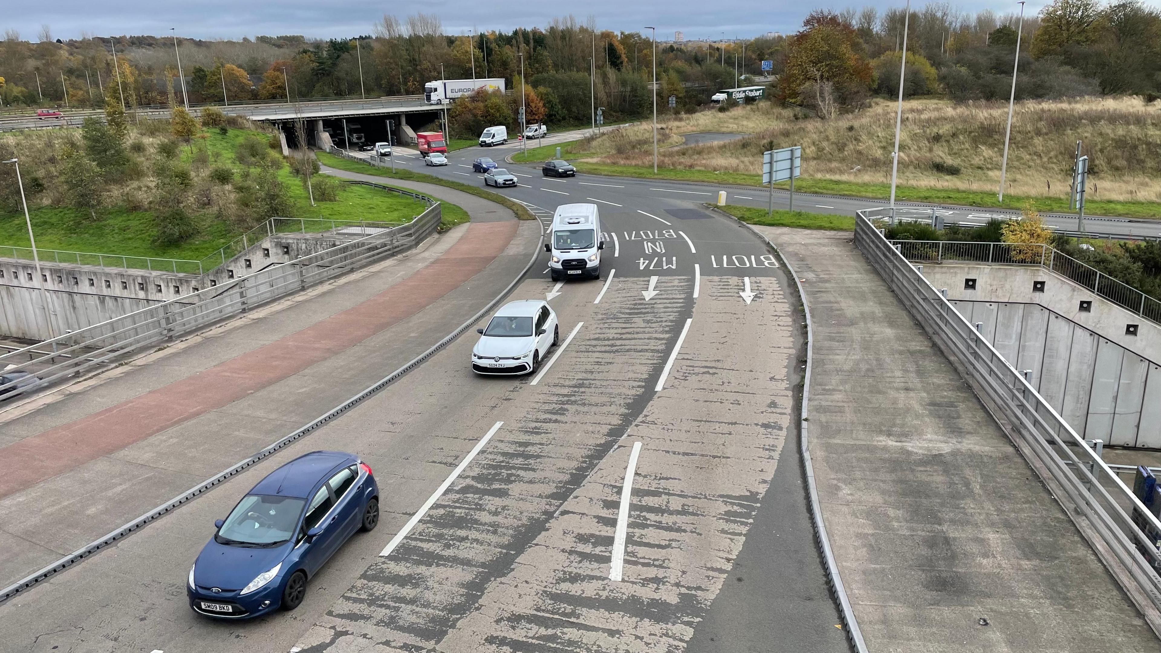 A junction on a motorway, with several cars and vans travelling along it