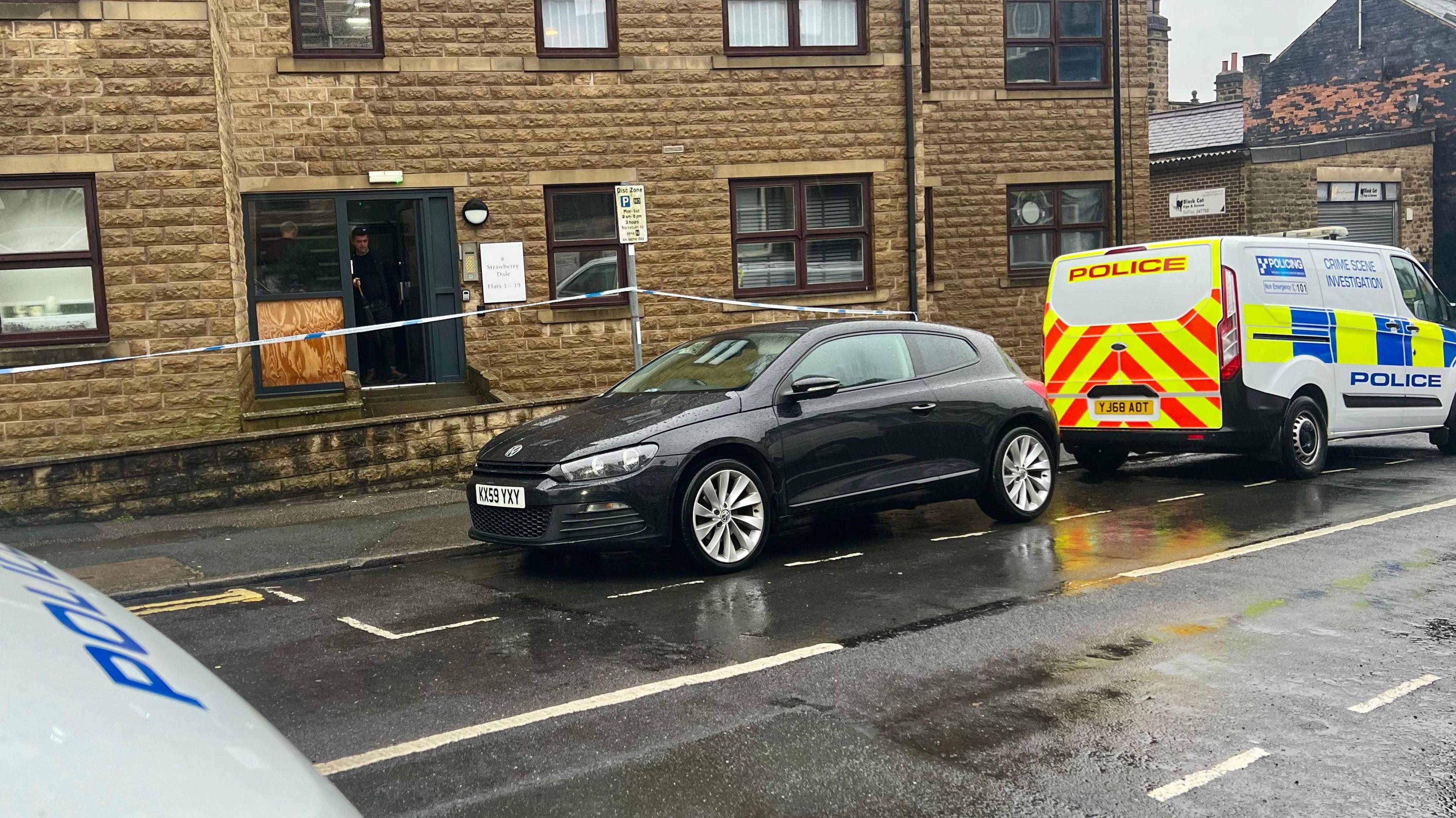 A car and a police van which reads "Crime Scene Investigation" outside a building with police tape outside.