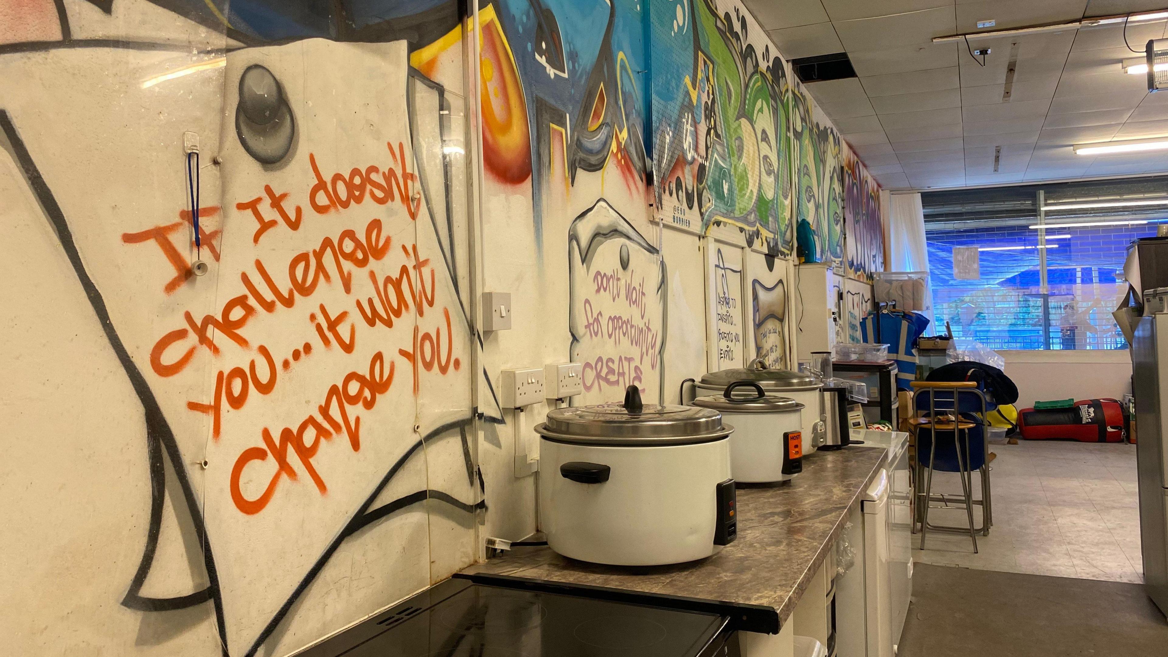 Pots and other cooking utensils in front of a wall with colourful artwork