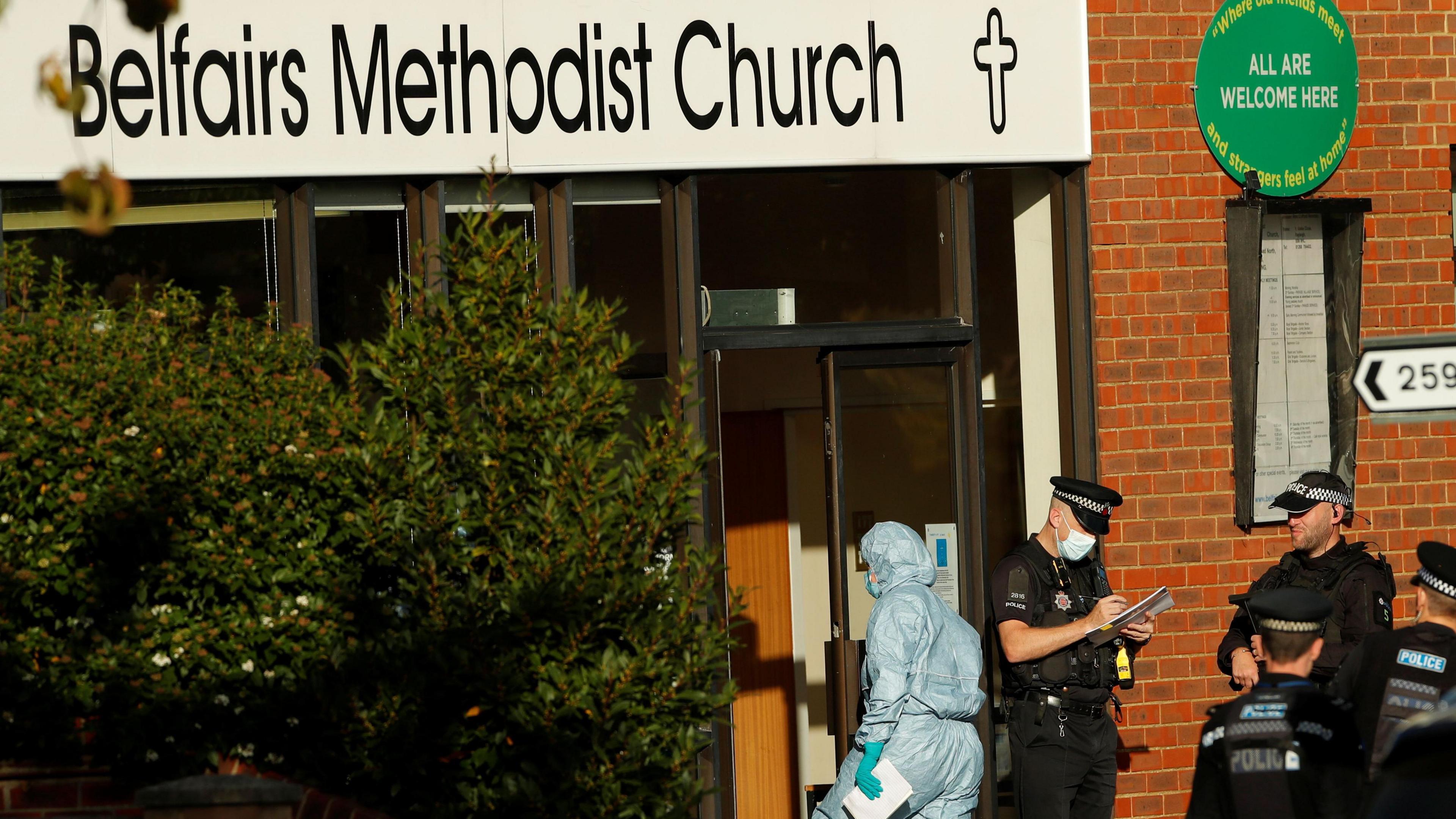 Forensics and police outside the church. One forensic worker is walking inside the church and two police officers are taking notes while standing outside