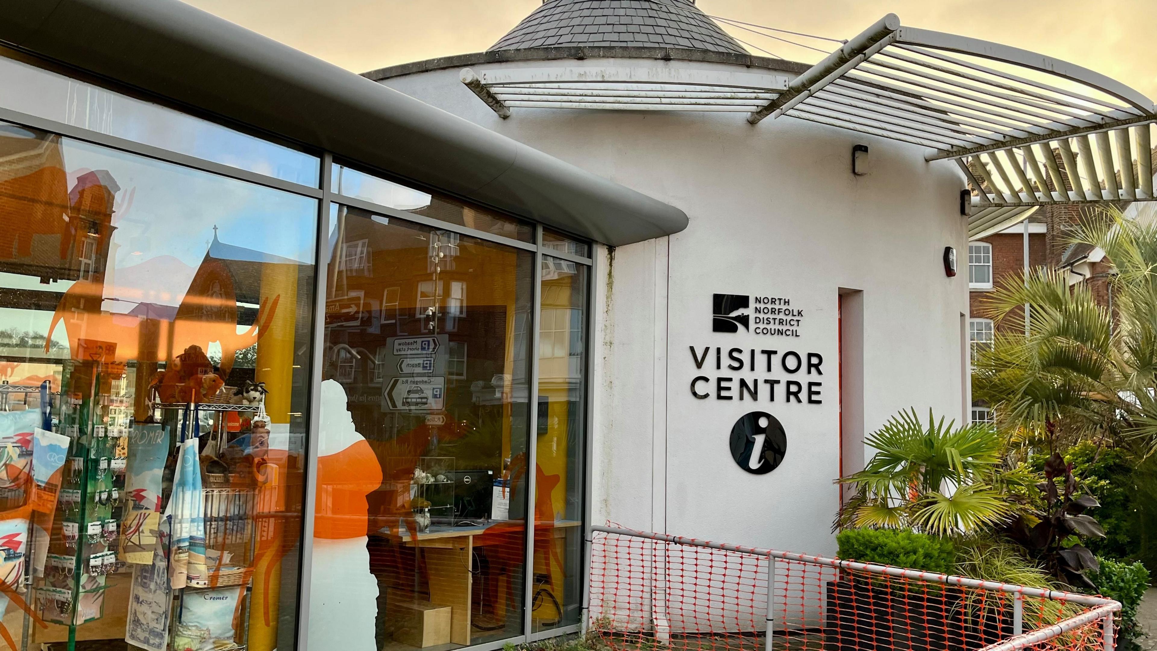 The picture shows the front of Cromer's visitor centre which has a white, circular wall and a glass window out on to the street.