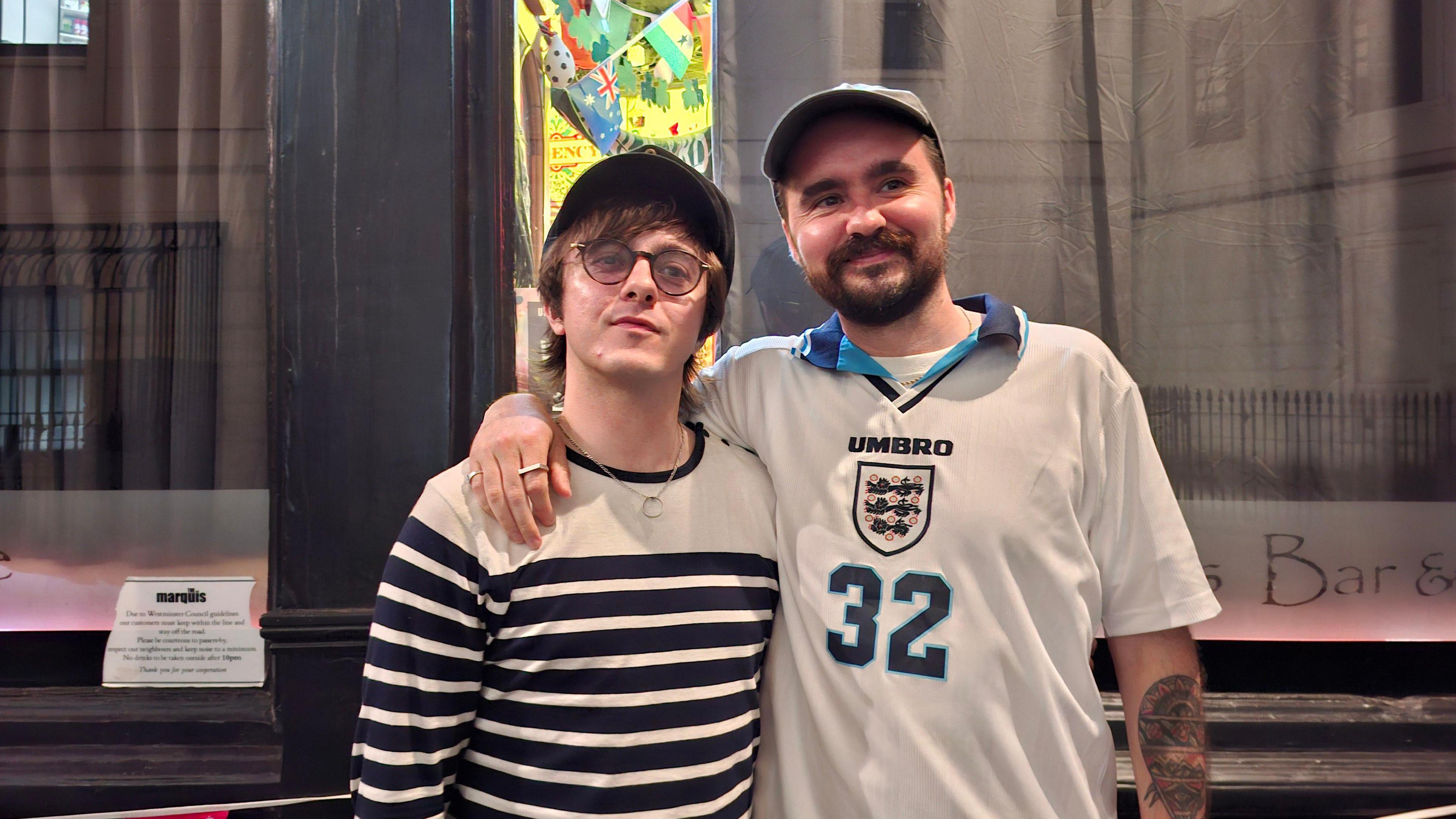 George Wright, wearing a Euro 96 England shirt with 32 on the front, puts his arm around his brother, Laurie, wearing a stripey long-sleeve t-shirt while standing outside a pub in central London. 