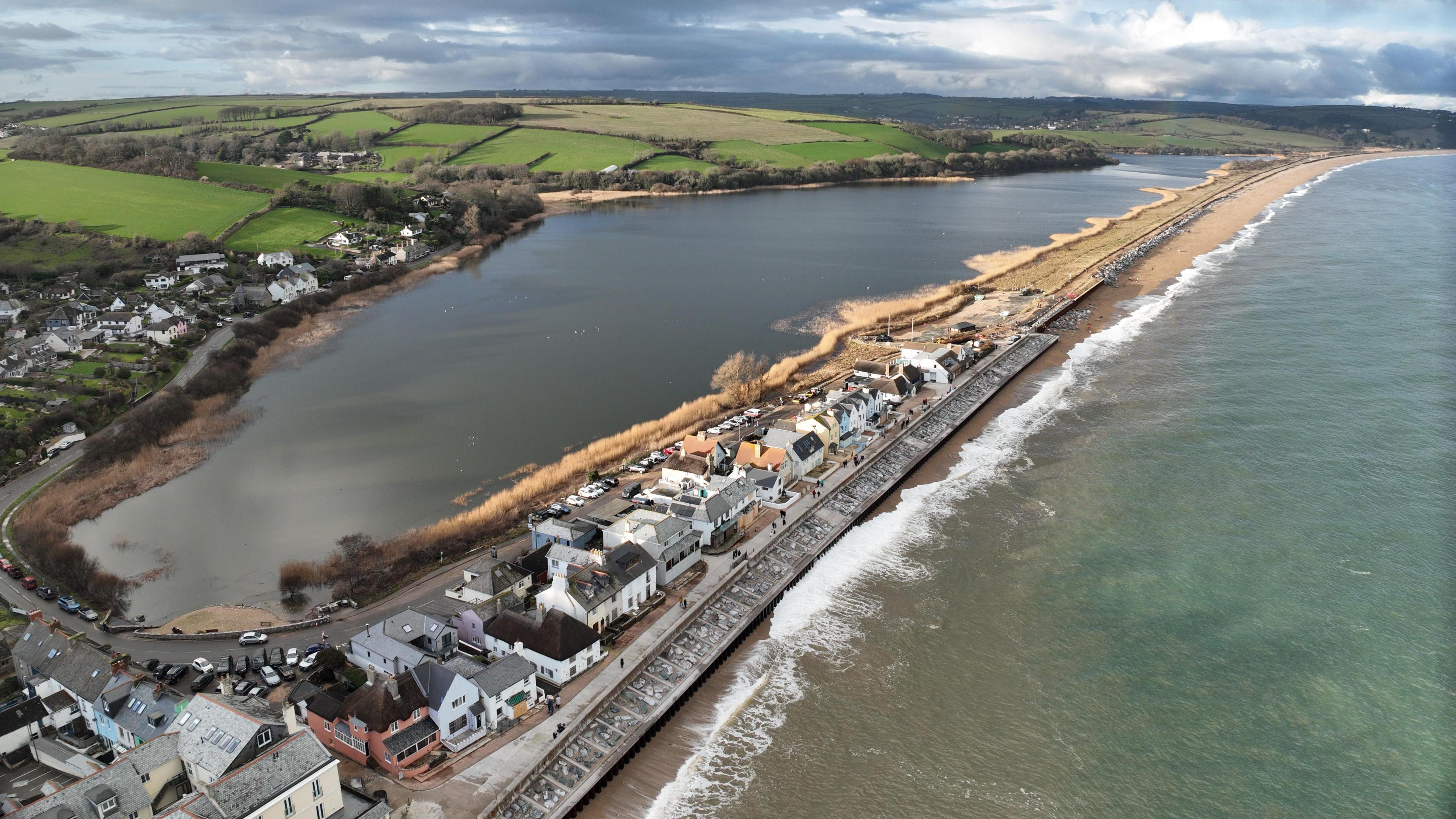 An aerial view of Torcross and Slapton beach in Devon - which saw huge waves during Storm Ingrid.  The road that runs across the shingle bar disappears into the distance.  In the foreground houses and other buildings are visible close t the waters edge, which is lined with concrete sea defences