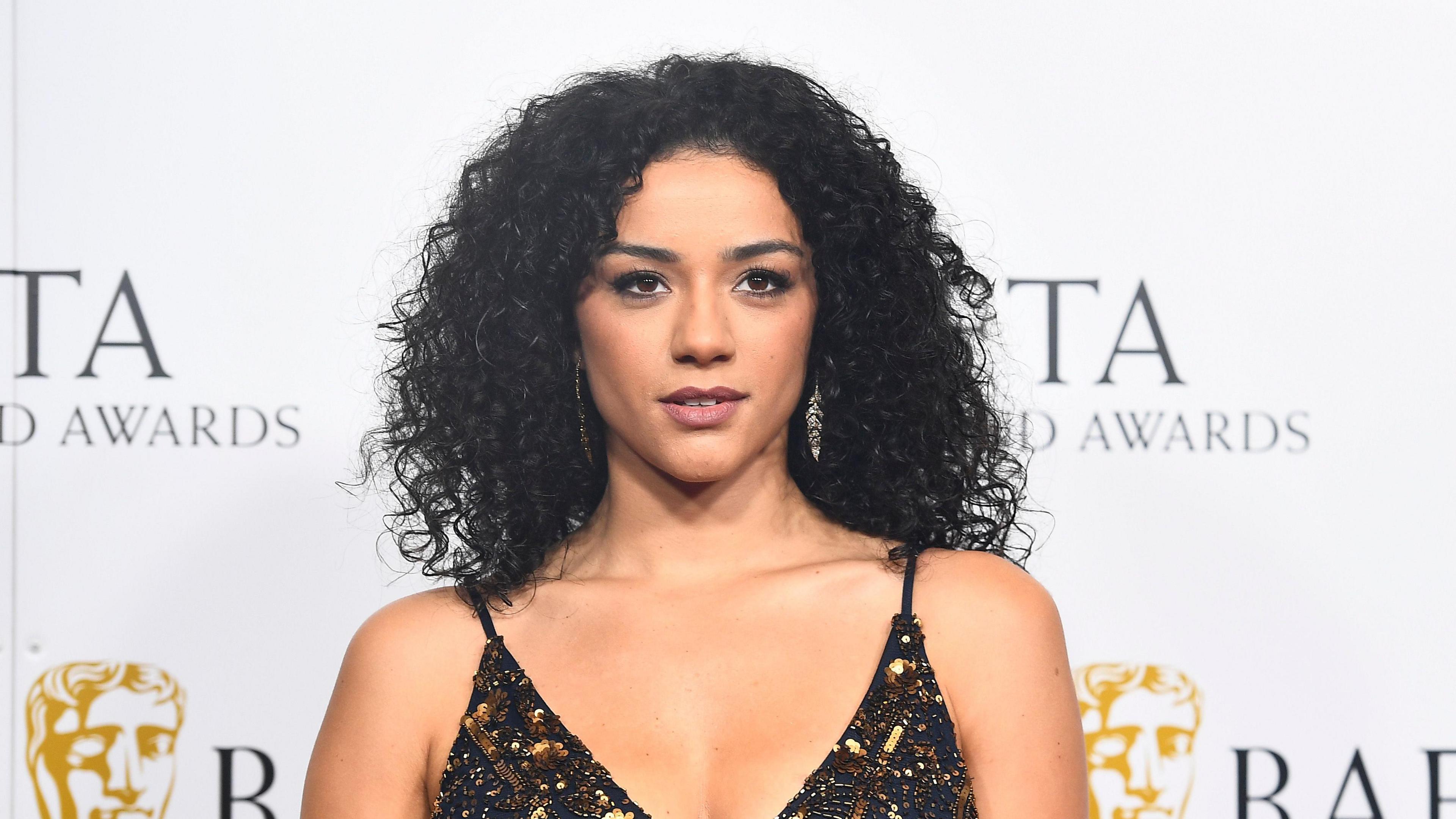Shereen Cutkelvin poses on the red carpet at an awards ceremony - she has shoulder length black hair and a black and gold dress on.