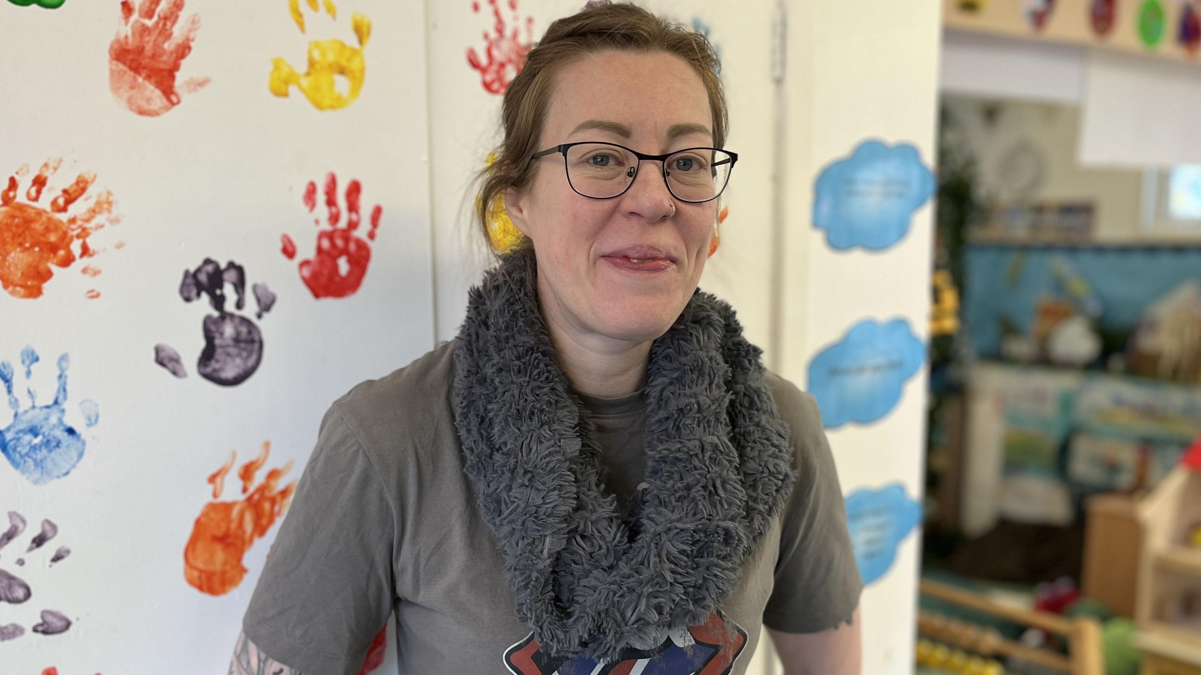 Voluntary treasurer and parent, Sarah Fox, smiling and standing in front of a wall covered in children's hand prints