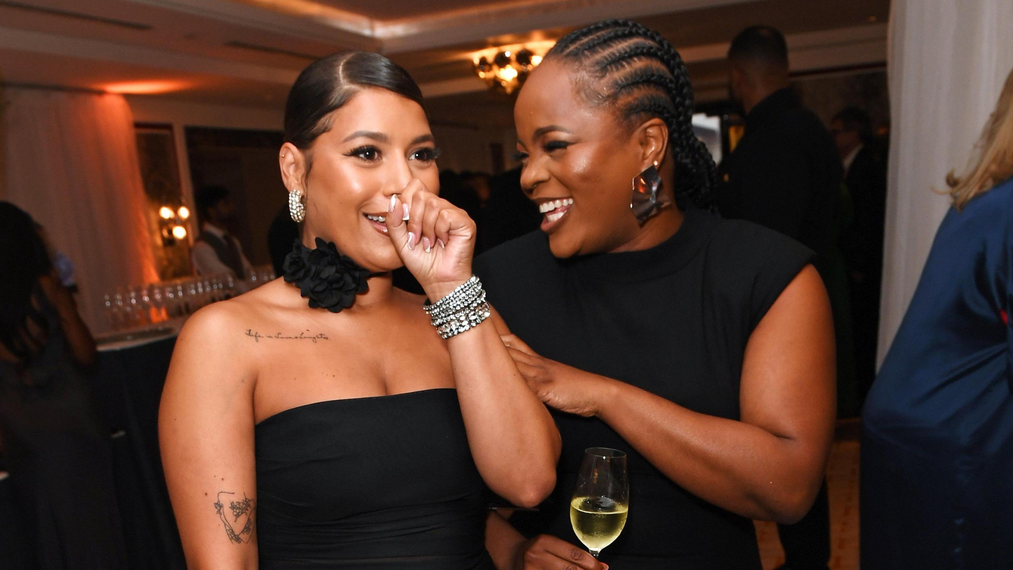 Milena pictured with former co-host Tolani Shoneye at a party in 2023. They are both dressed in black and Milena, left, holds her hand to her face as she laughs as Tolani also smiles beside her, her hand on her arm. 