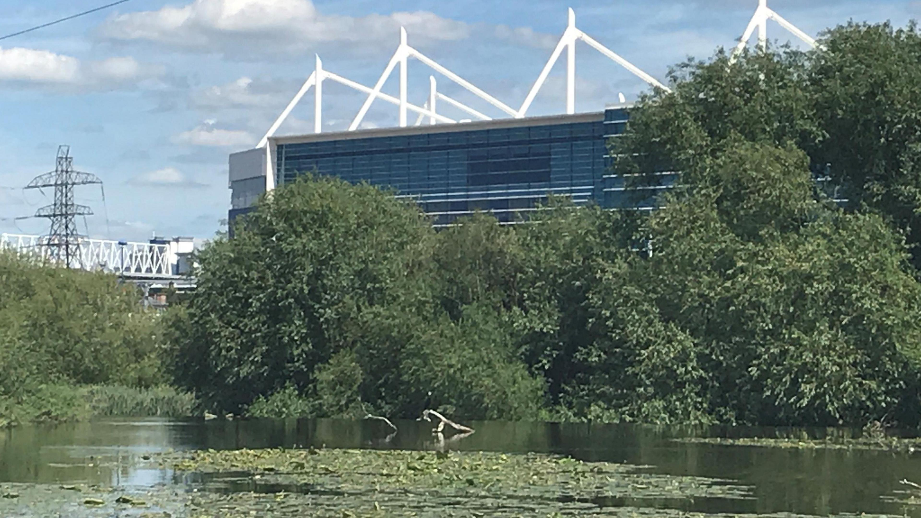 A football stadium behind a river and trees