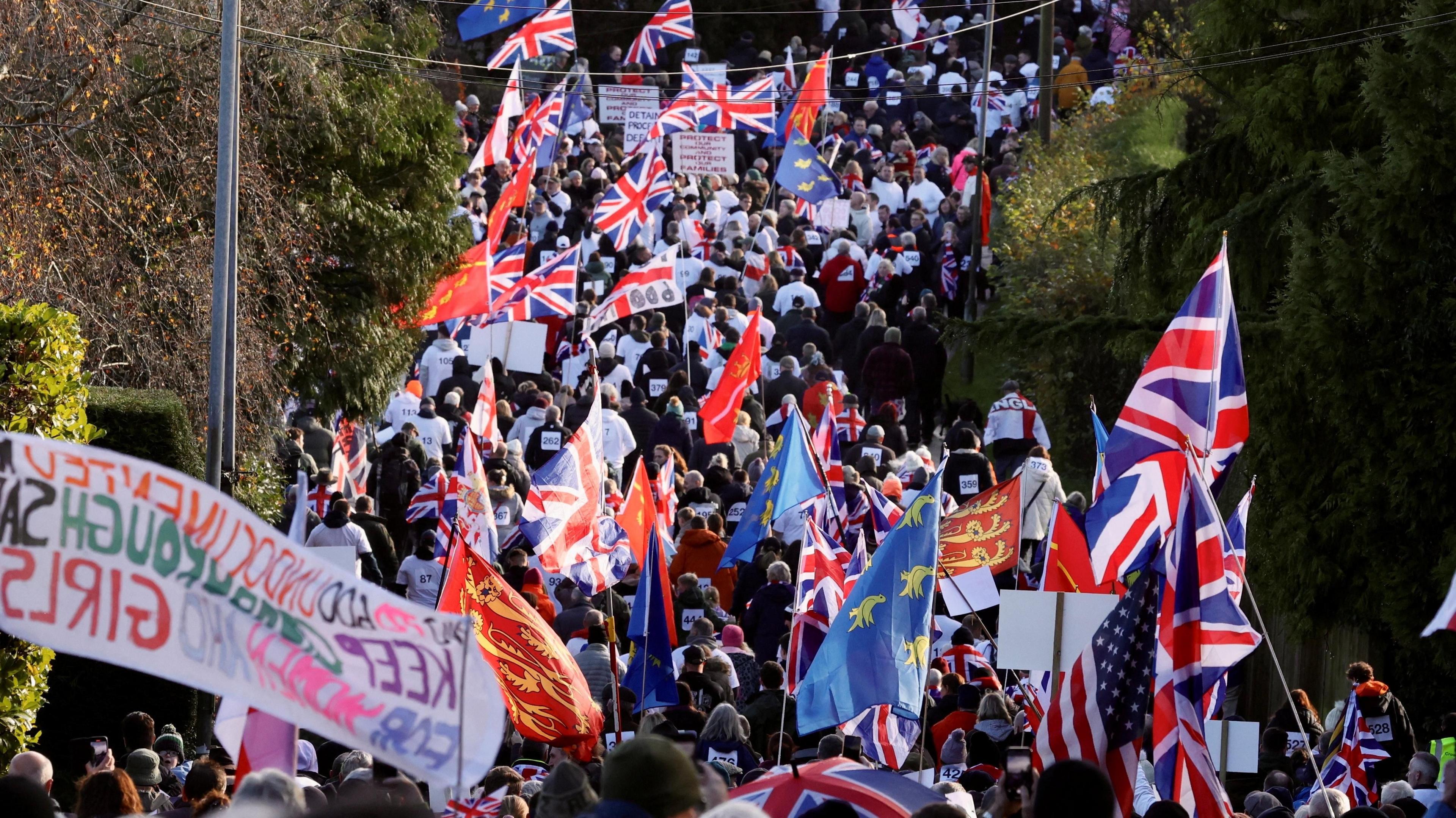 A large group of protestors. They are holding Union Jack and local flags. 