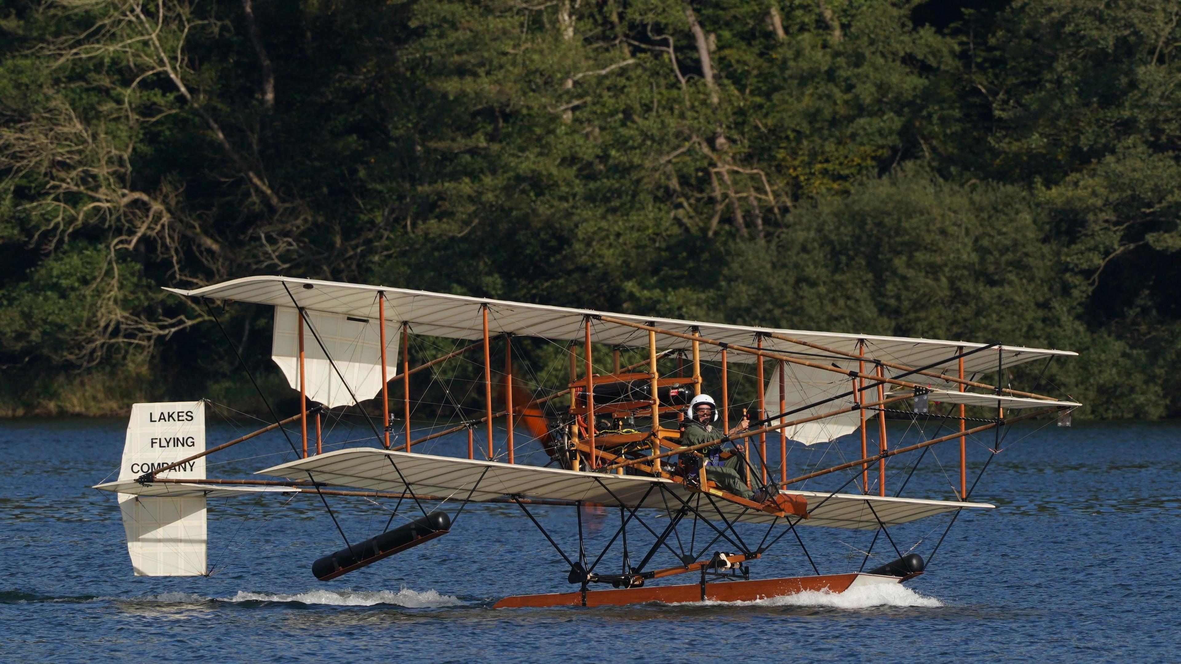 A pilot wearing a helmet in a white seaplane on a lake in 2022.