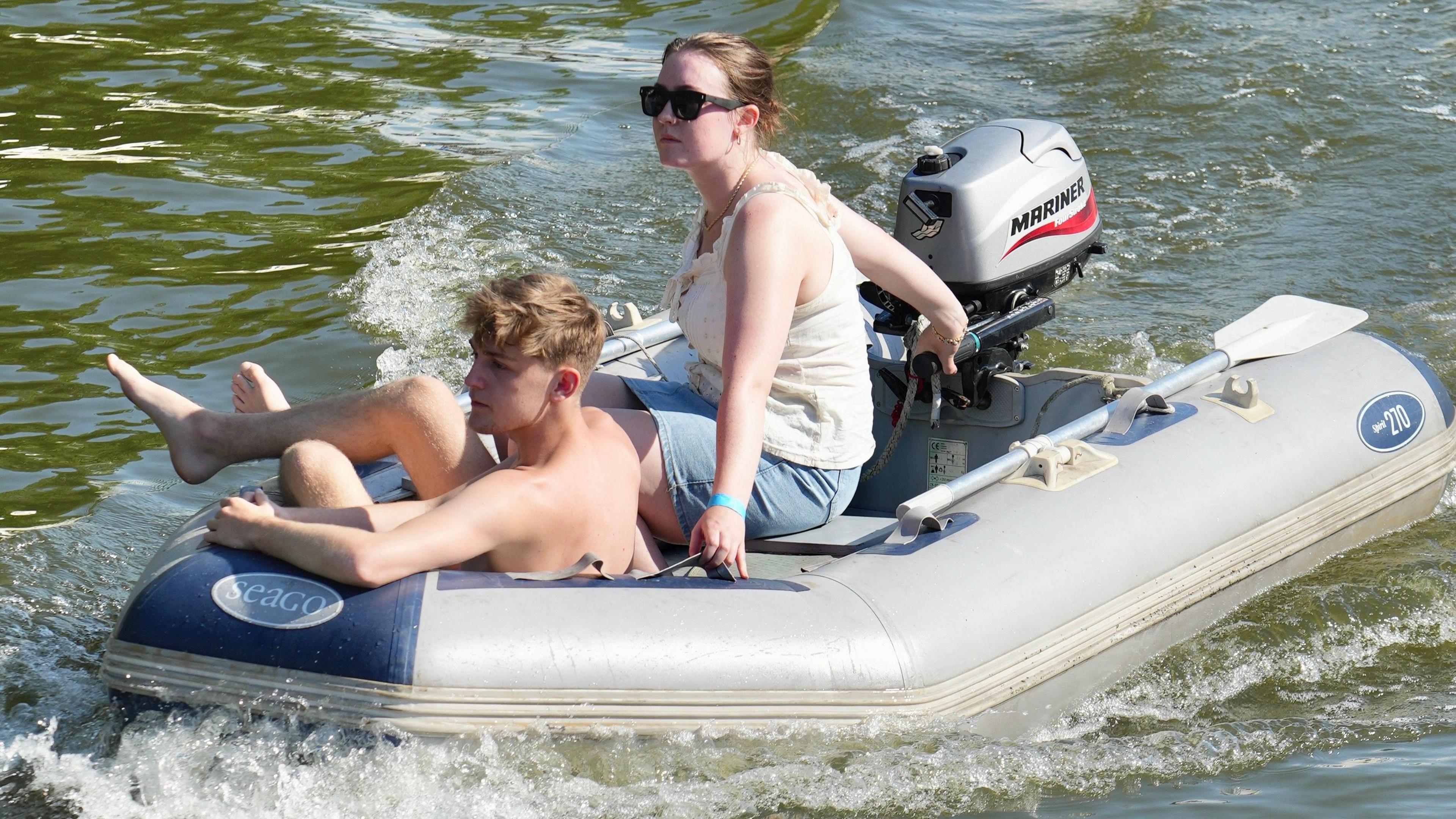 Two people in a boat. A man is relaxing with his legs over the side of the boat, whilst a woman sits next to him controlling the boat. 