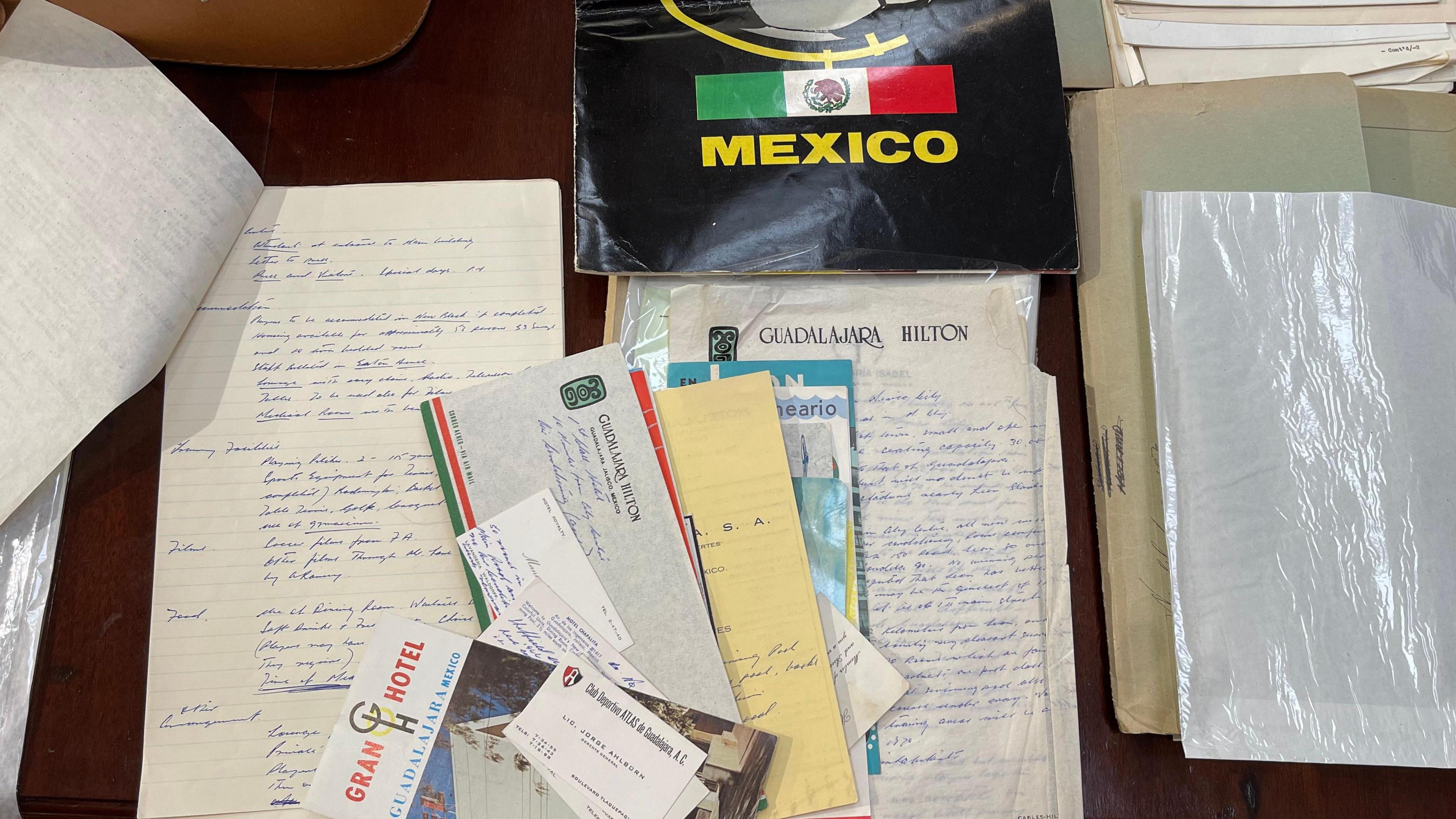 An assortment of documents on a wooden table. Notes have been written on the backs of business cards and hotel paper