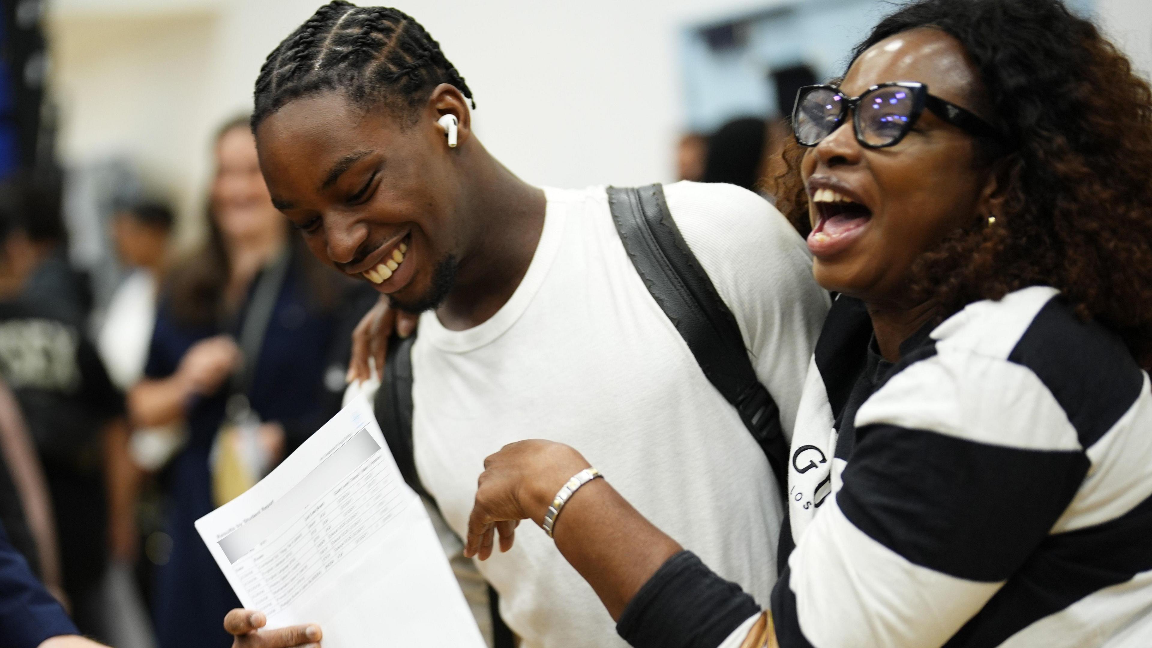 Two radical   clasp  a expanse  of insubstantial  portion    lasting  successful  a crowded indoor venue. A 3rd  idiosyncratic   is partially disposable   beside them. Other students are picking up   their results down  them, appearing blurred successful  the background.