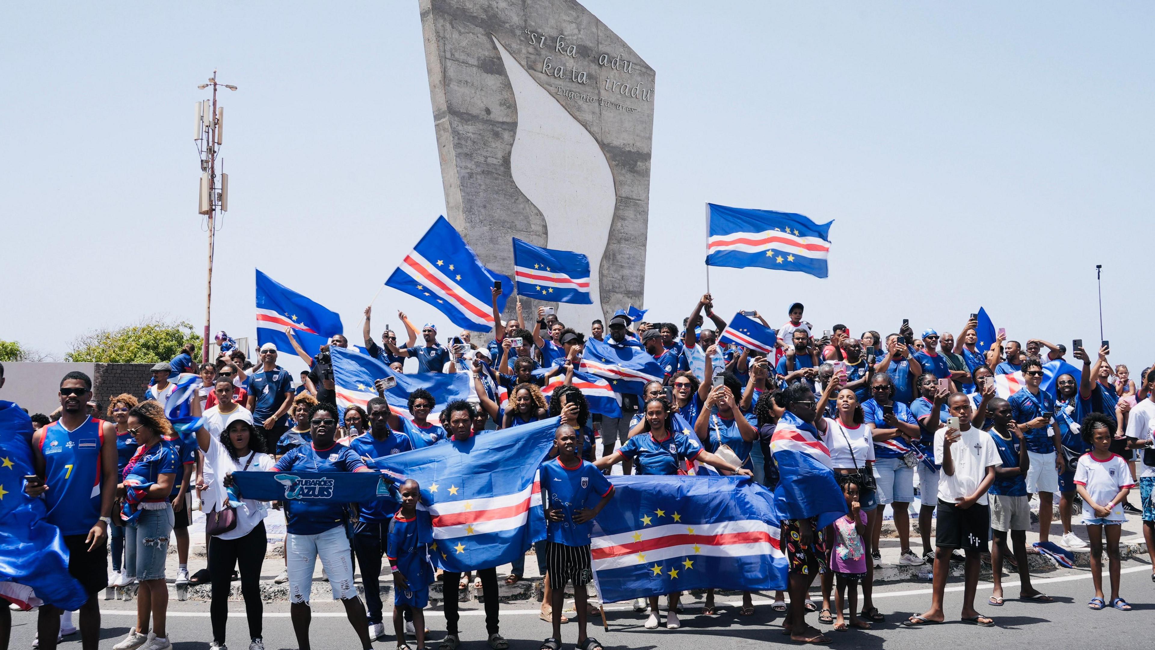 A group of fans, wearing the blue national kit, wave Cape Verde flags.