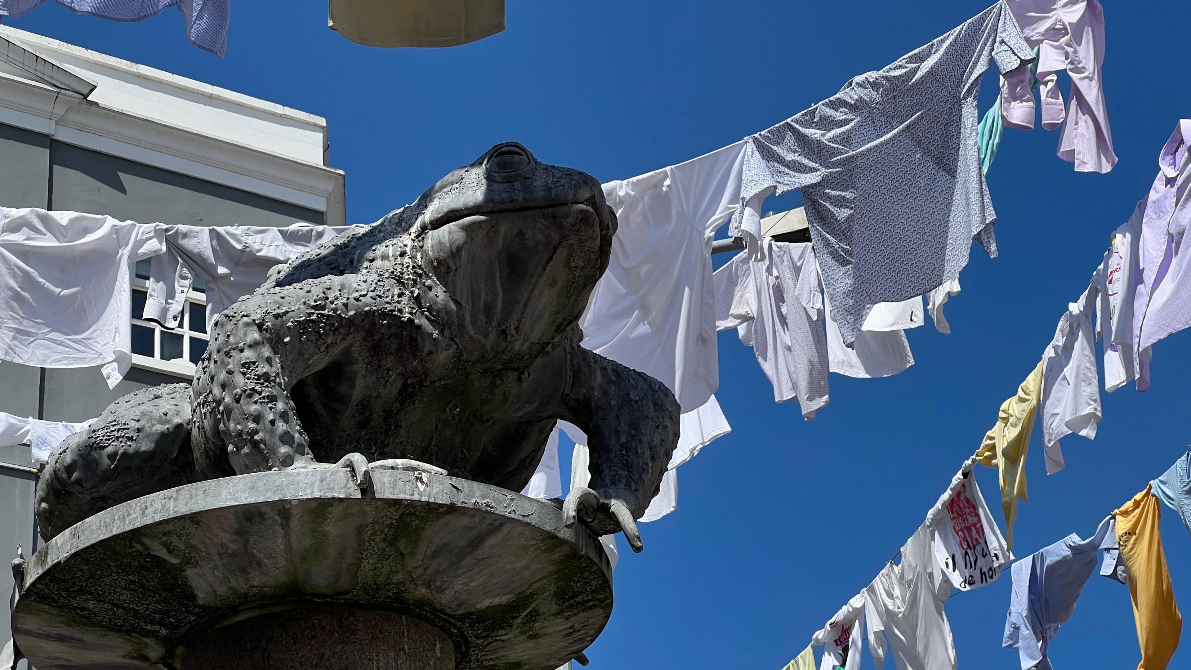 Shirts hang over the street which includes a statue of a toad