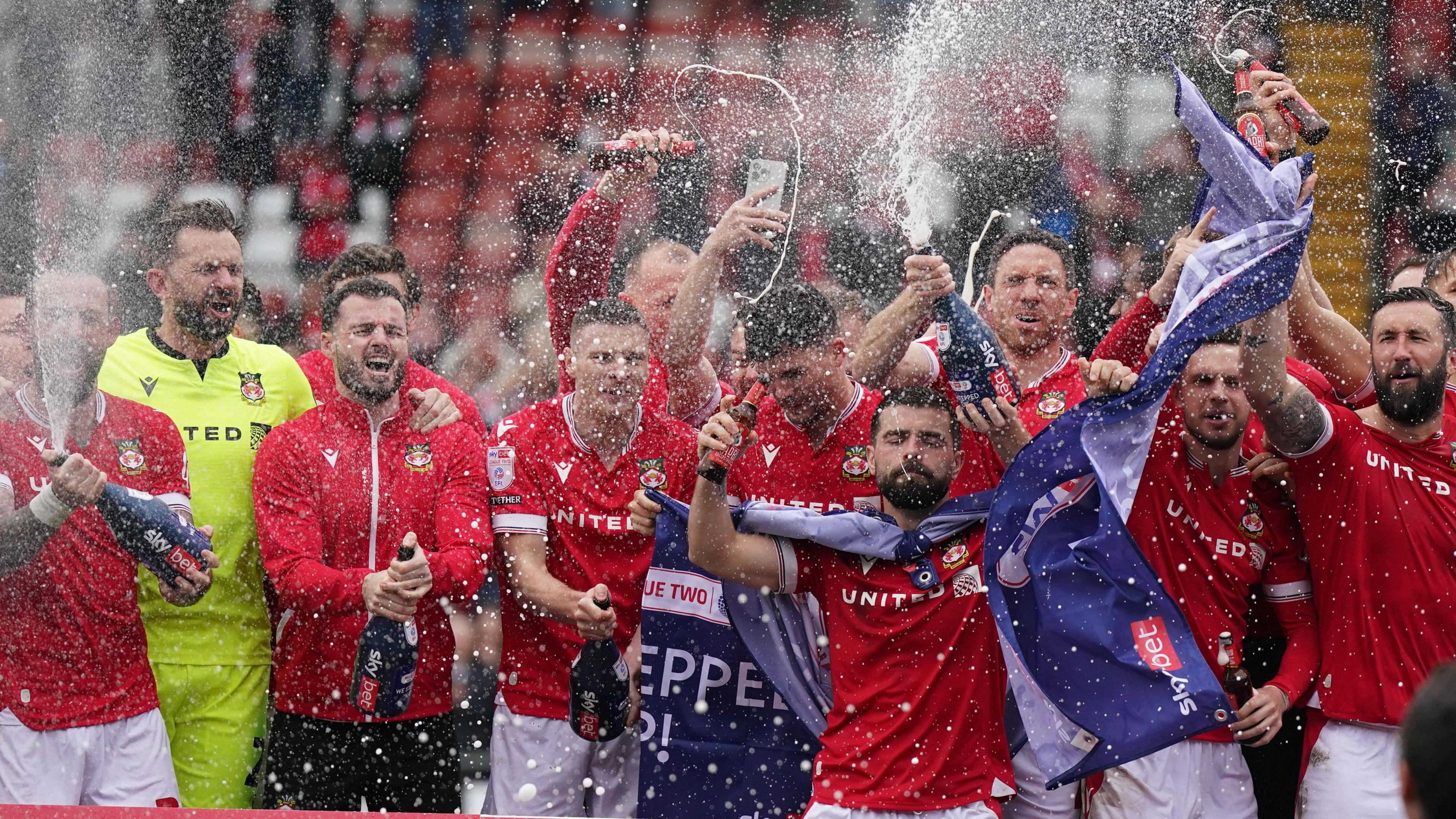 Wrexham players on the pitch celebrating promotion to League One after the final whistle of the Sky Bet League Two match at the SToK Cae Ras, Wrexham, in April 2024