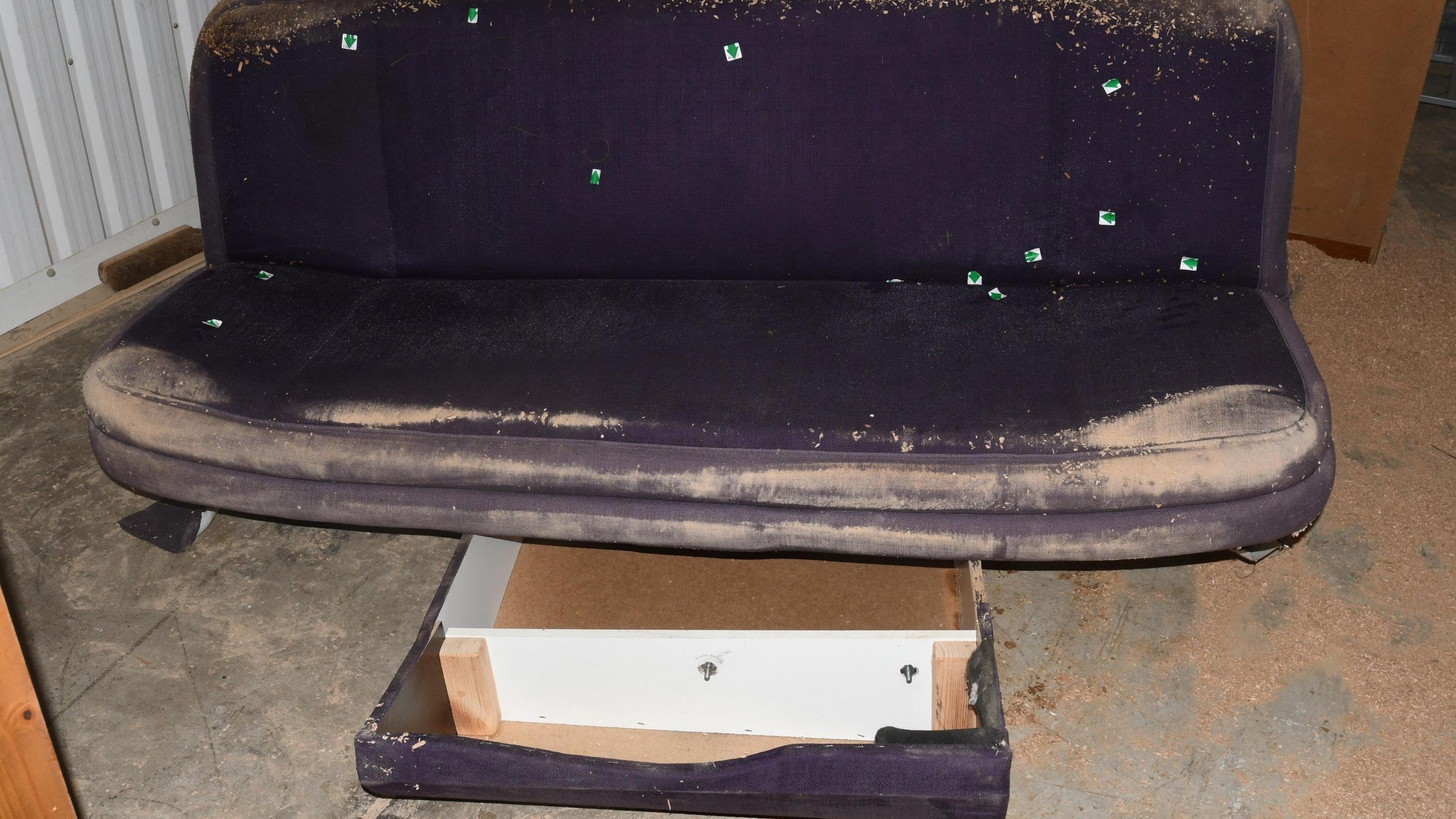 A dirty and battered brown sofa bed with a drawer underneath recovered by police.