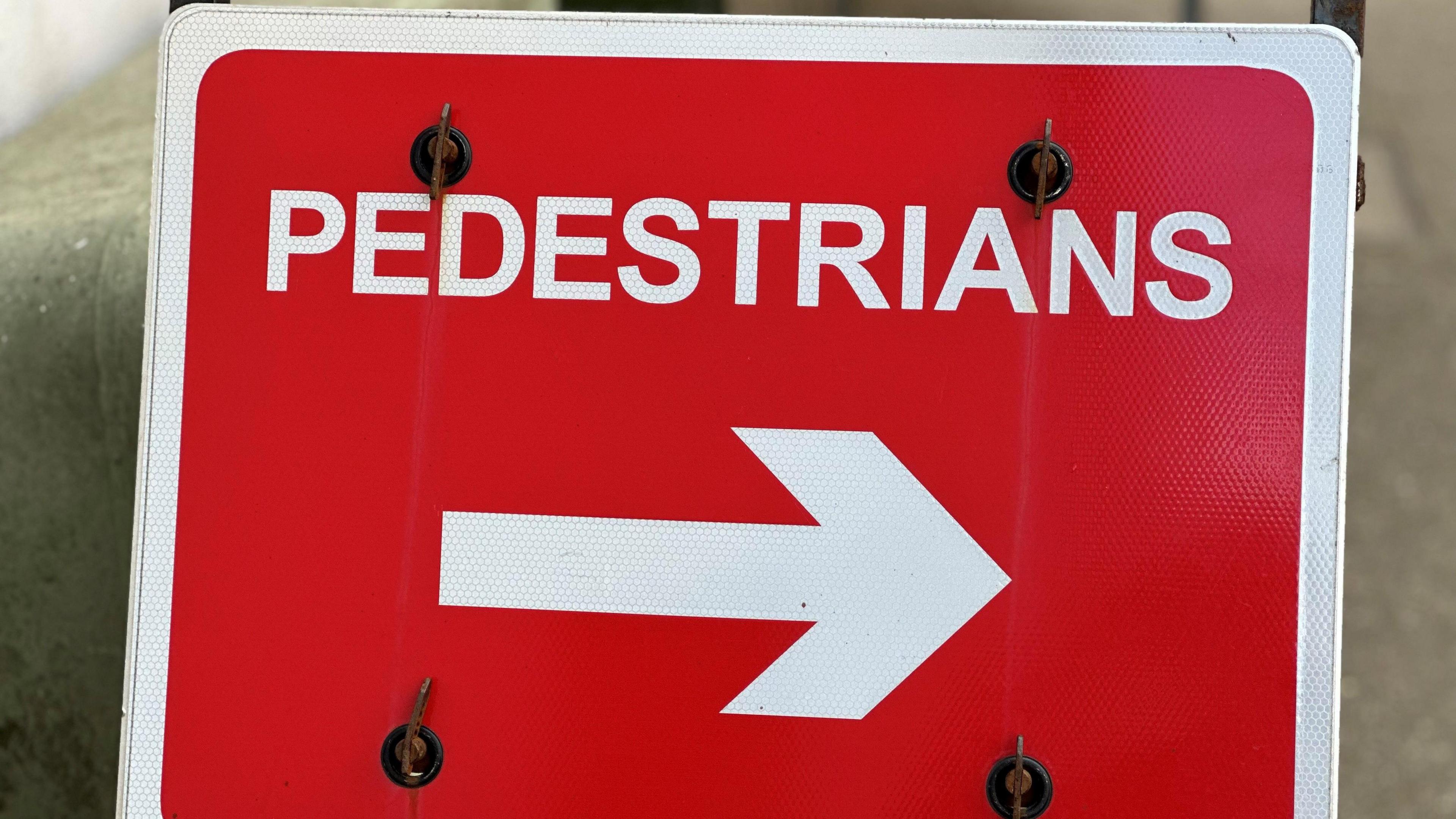 A closeup of a red sign with a white arrow pointing to the right in the centre that has the word Pedestrian written in white above it.