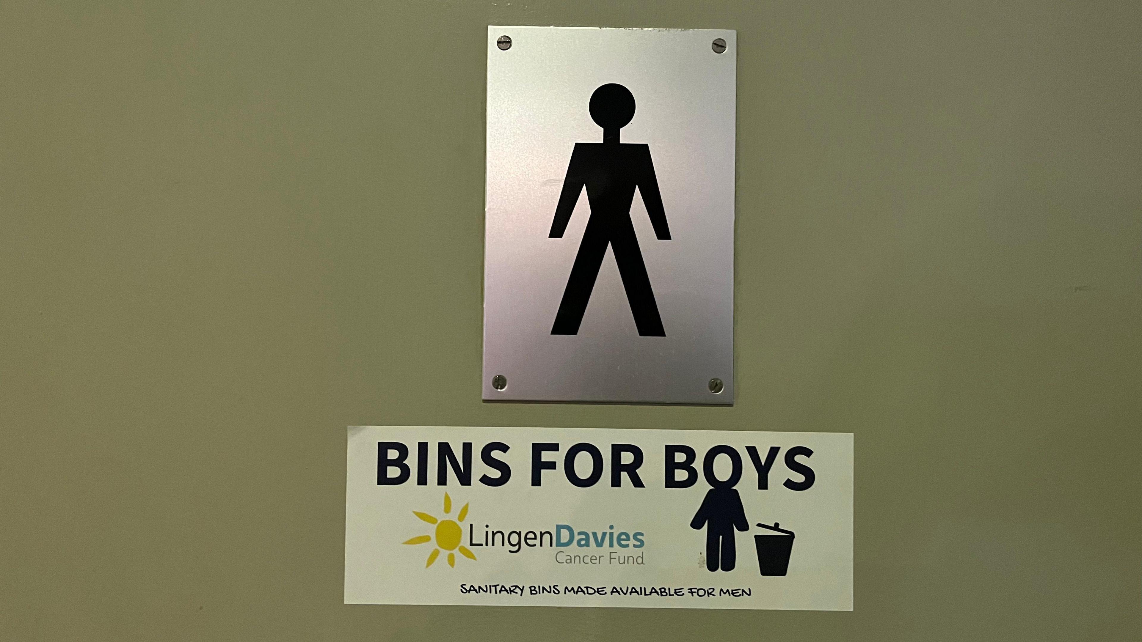 A green toilet door with a silver and black men's symbol on it. Underneath is a sticker that says "Bins for Boys, Lingen Davies Cancer Fund"