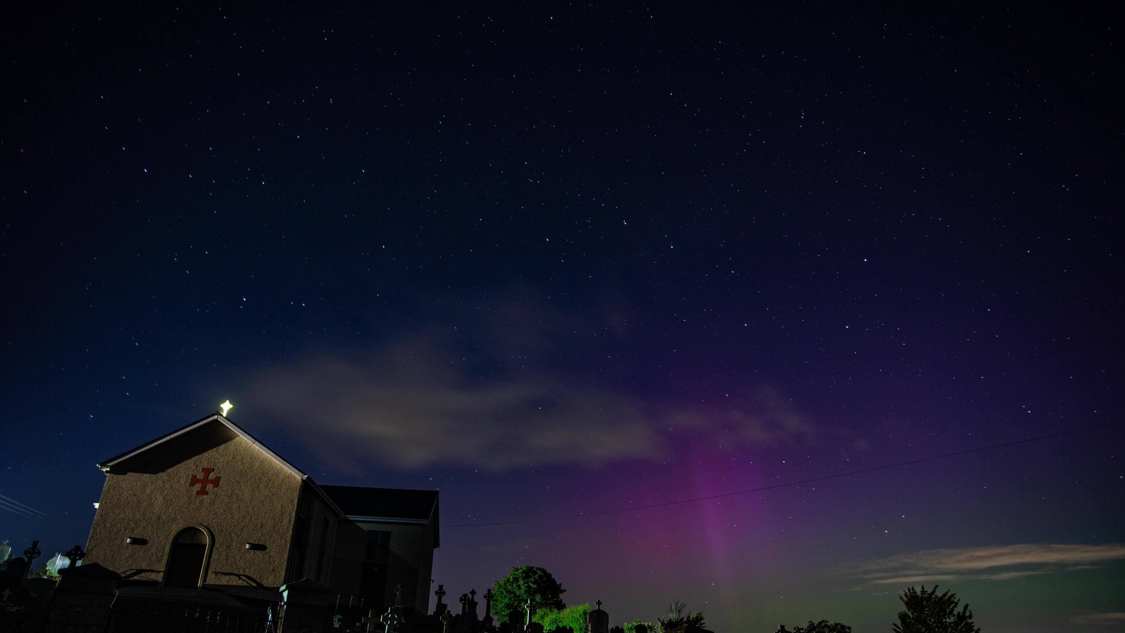 A church sits in the foreground of the northern lights