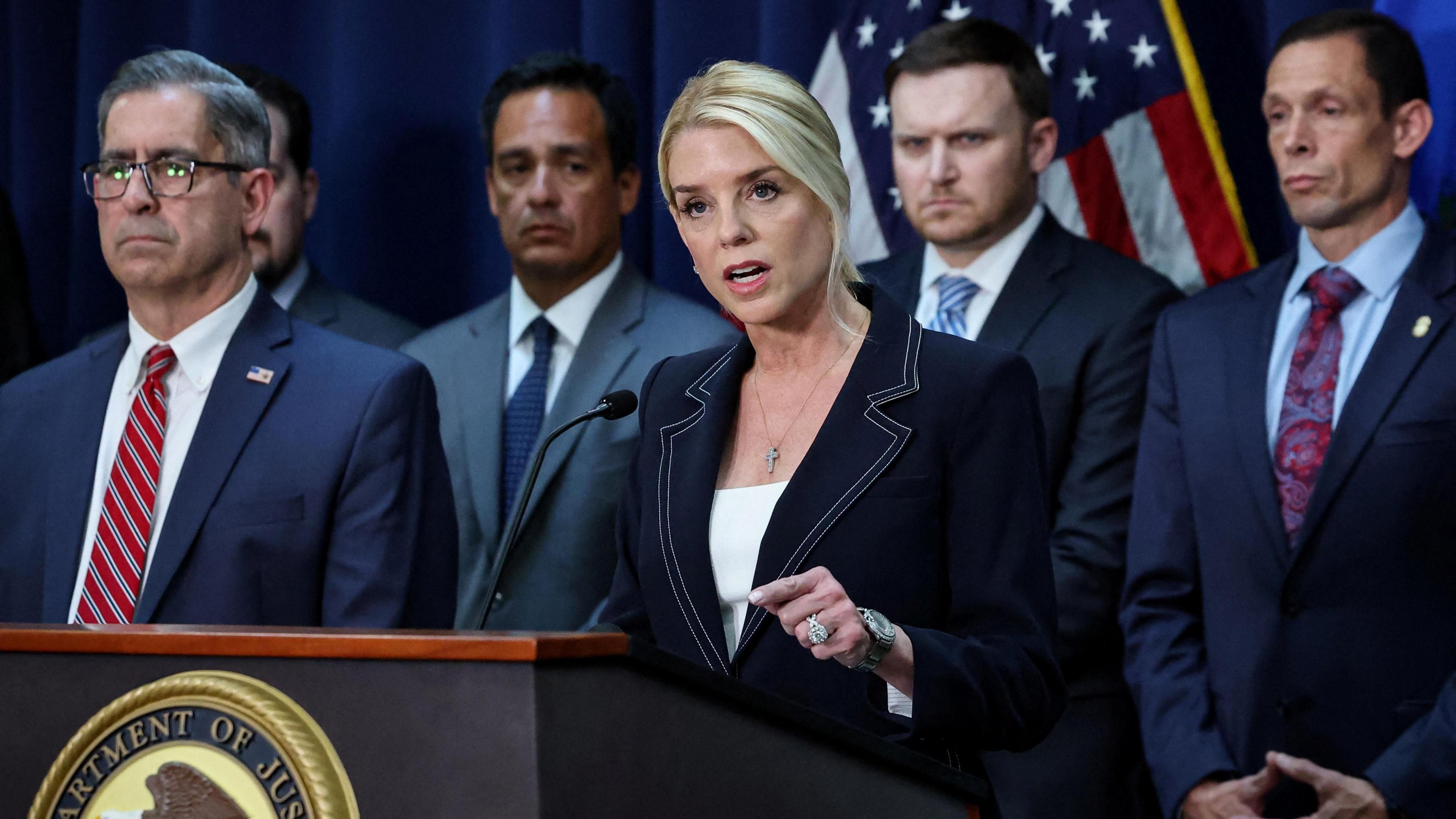 Pam Bondi wears a blue suit and is flanked by men in suits