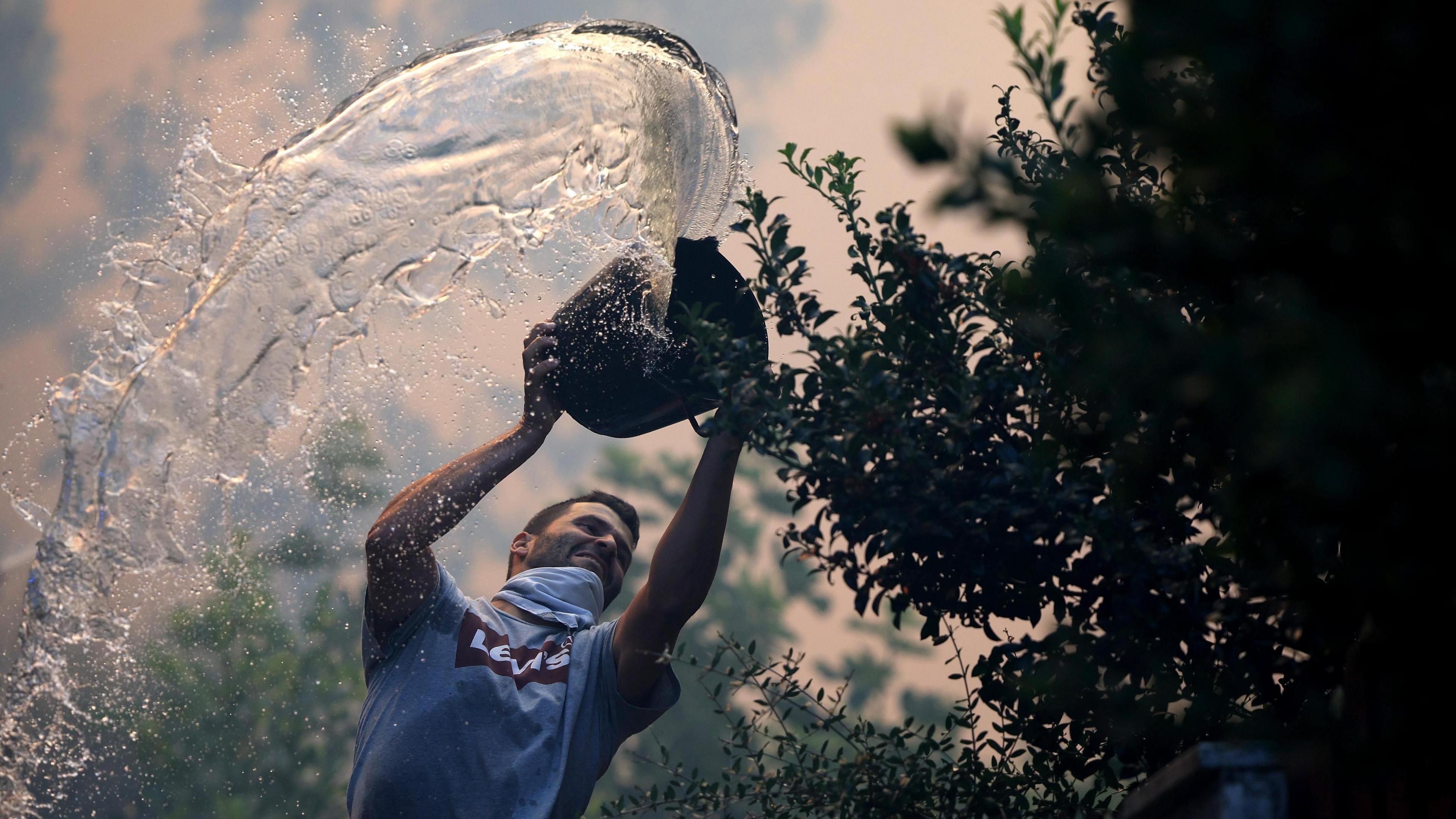 A man throws a bucket of water as he fights a forest fire in Macinhata da Seixa, Oliveira de Azemeis, Agueda, Portugal