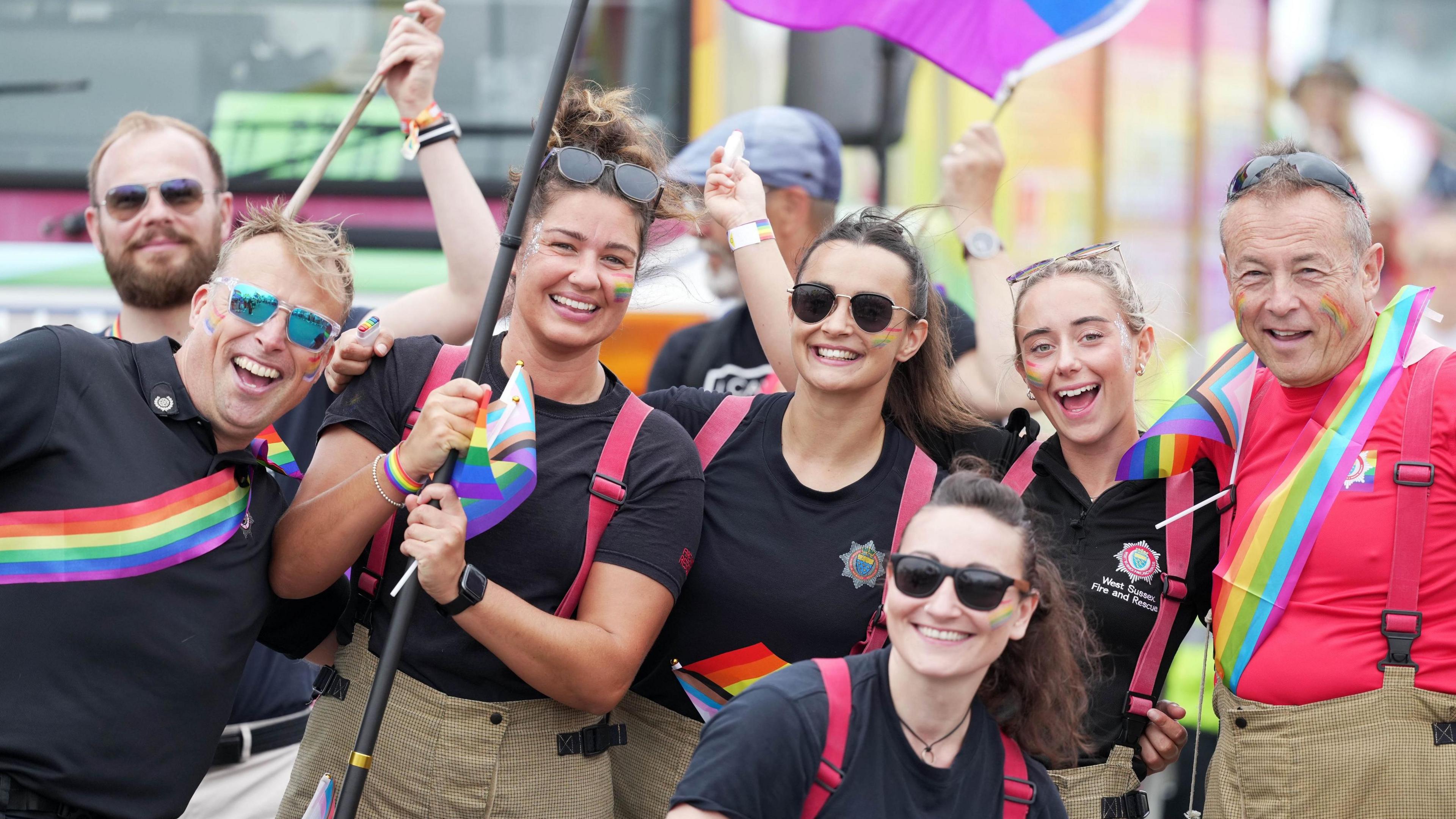 Six people from Crews from West Sussex Fire and Rescue Service in the parade. Five in black shirts with a rainbow stripe, one man on the right with a red shirt and rainbow stripe