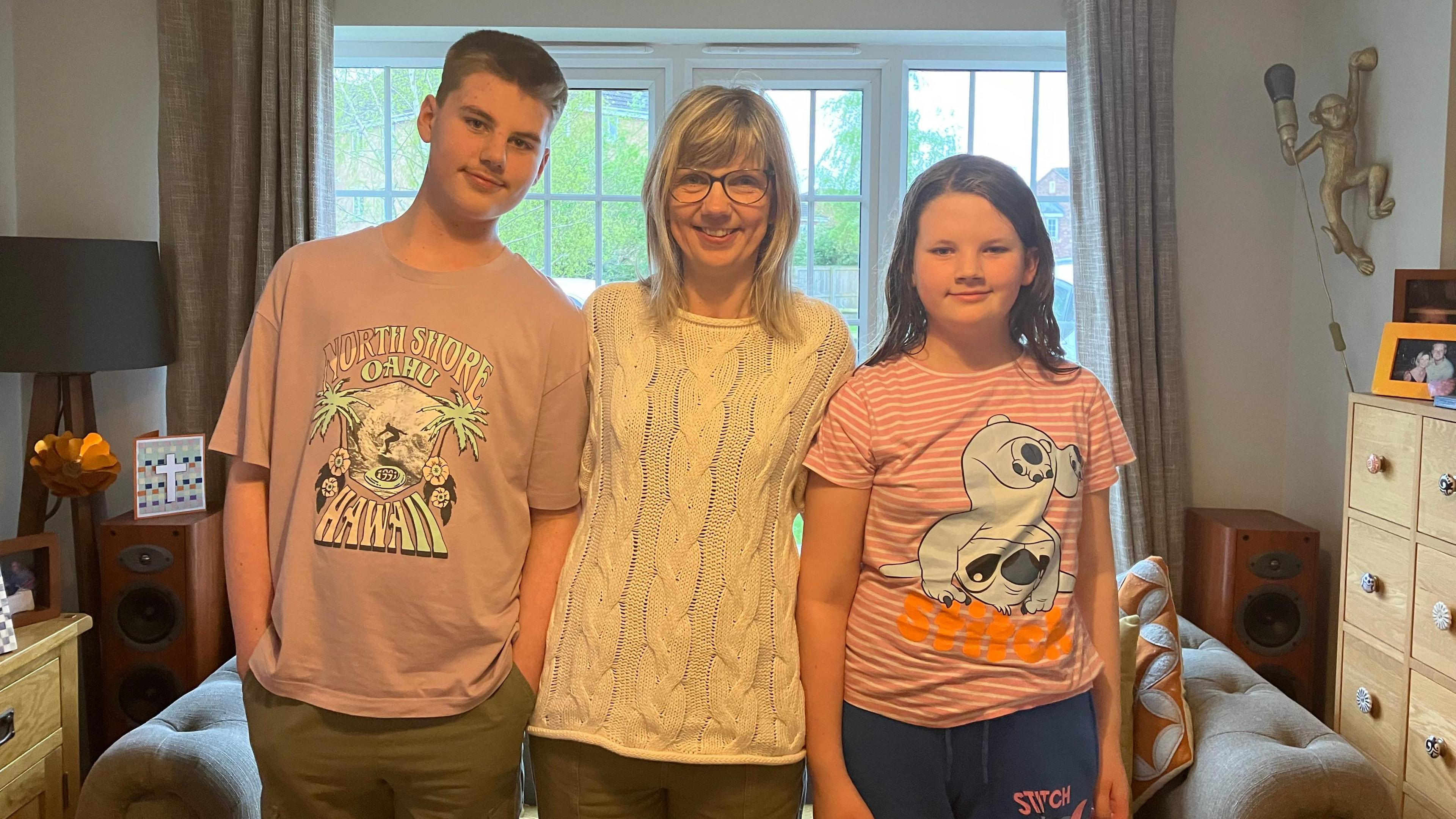 12 year old Jakob, stands next to his mum Catherine and 11 year old sister Eliana in their home