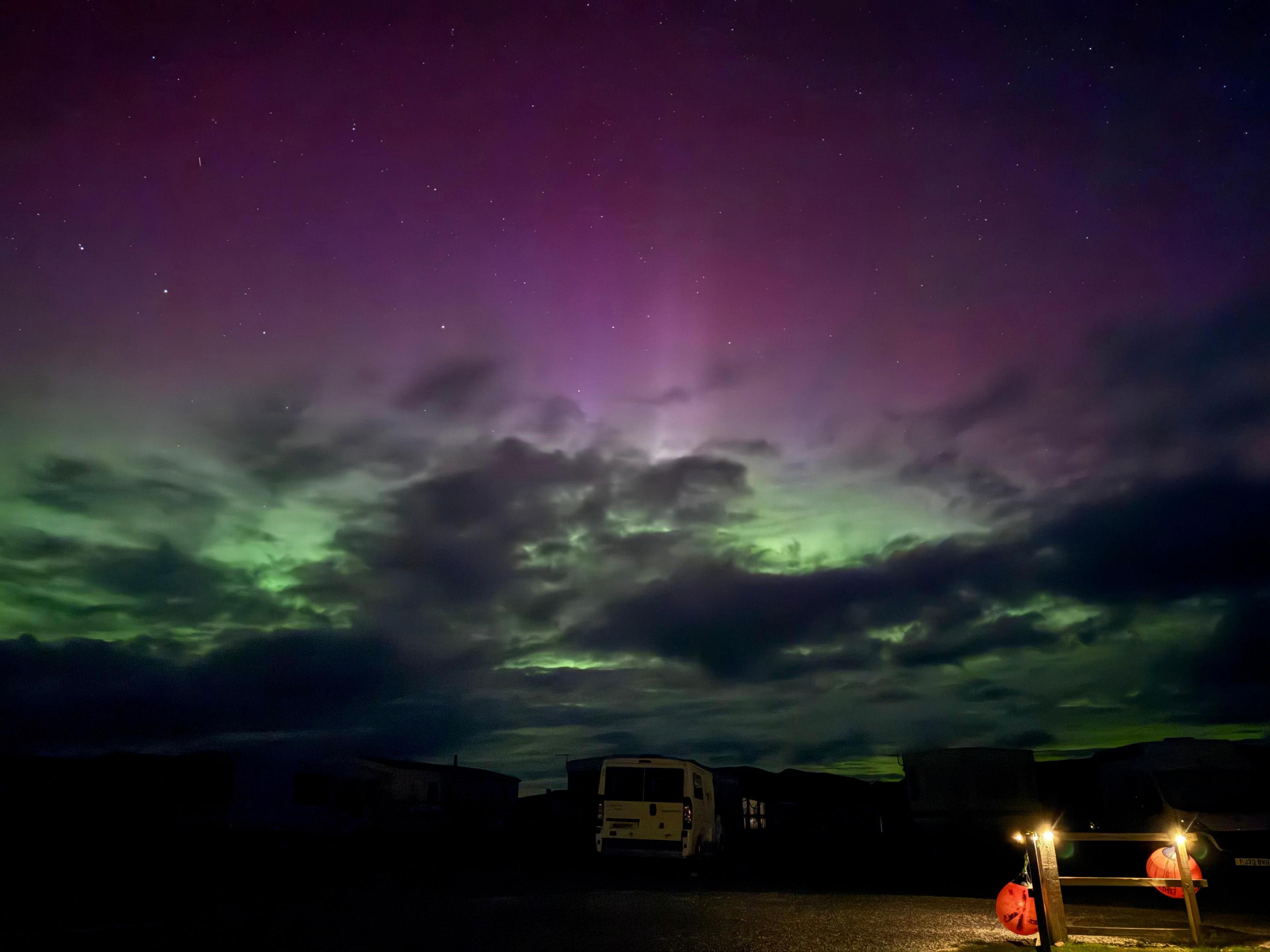 The Northern Lights are seen in the early hours of Wednesday morning in the village of Clachtoll in the Highlands. A van is parked in the picture but is barely visible in the dark of night. Lights on a fence glow in the bottom right of the photo.