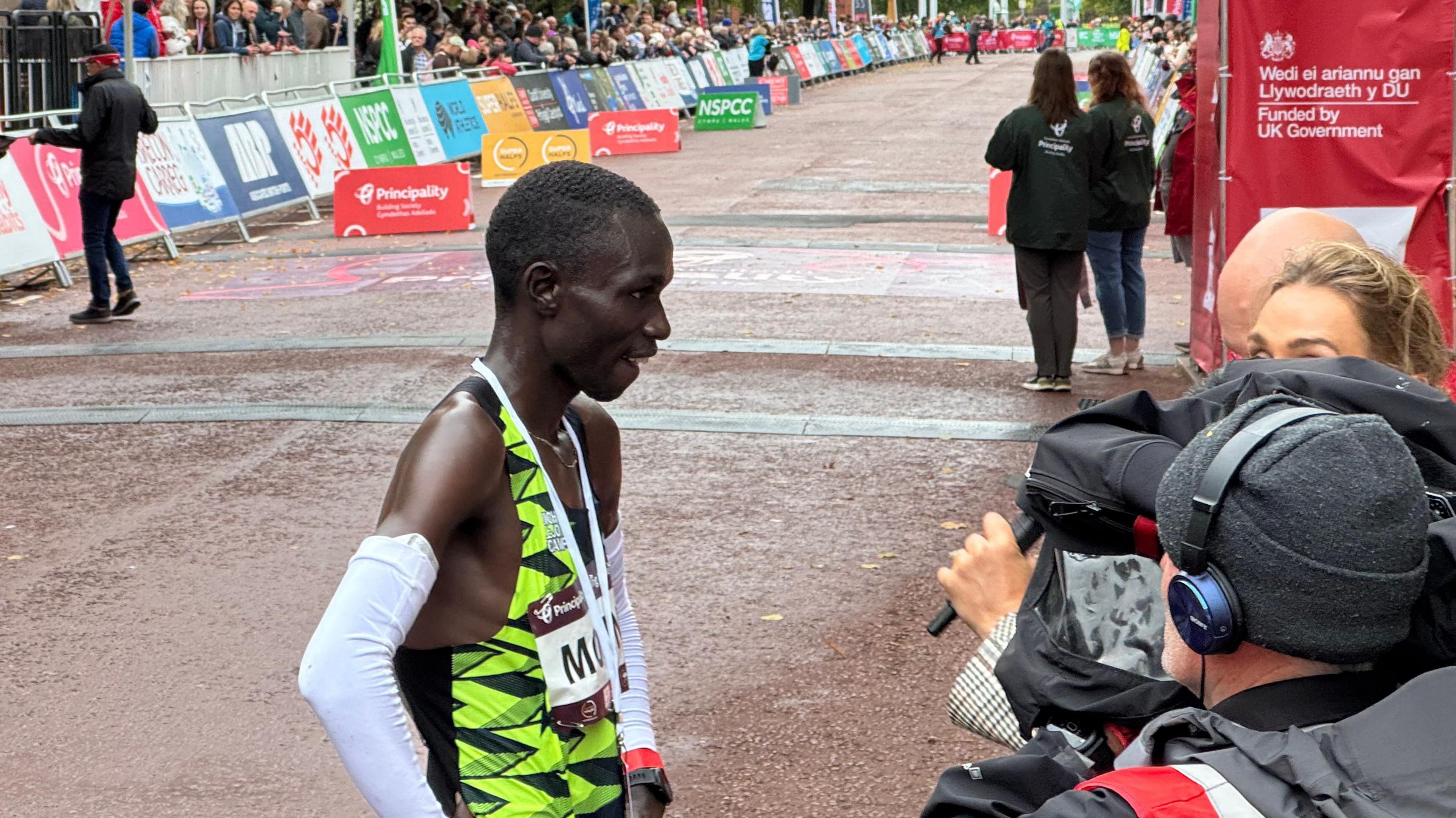 Patrick Moisin speaks with a camera crew beneath the finish line clock