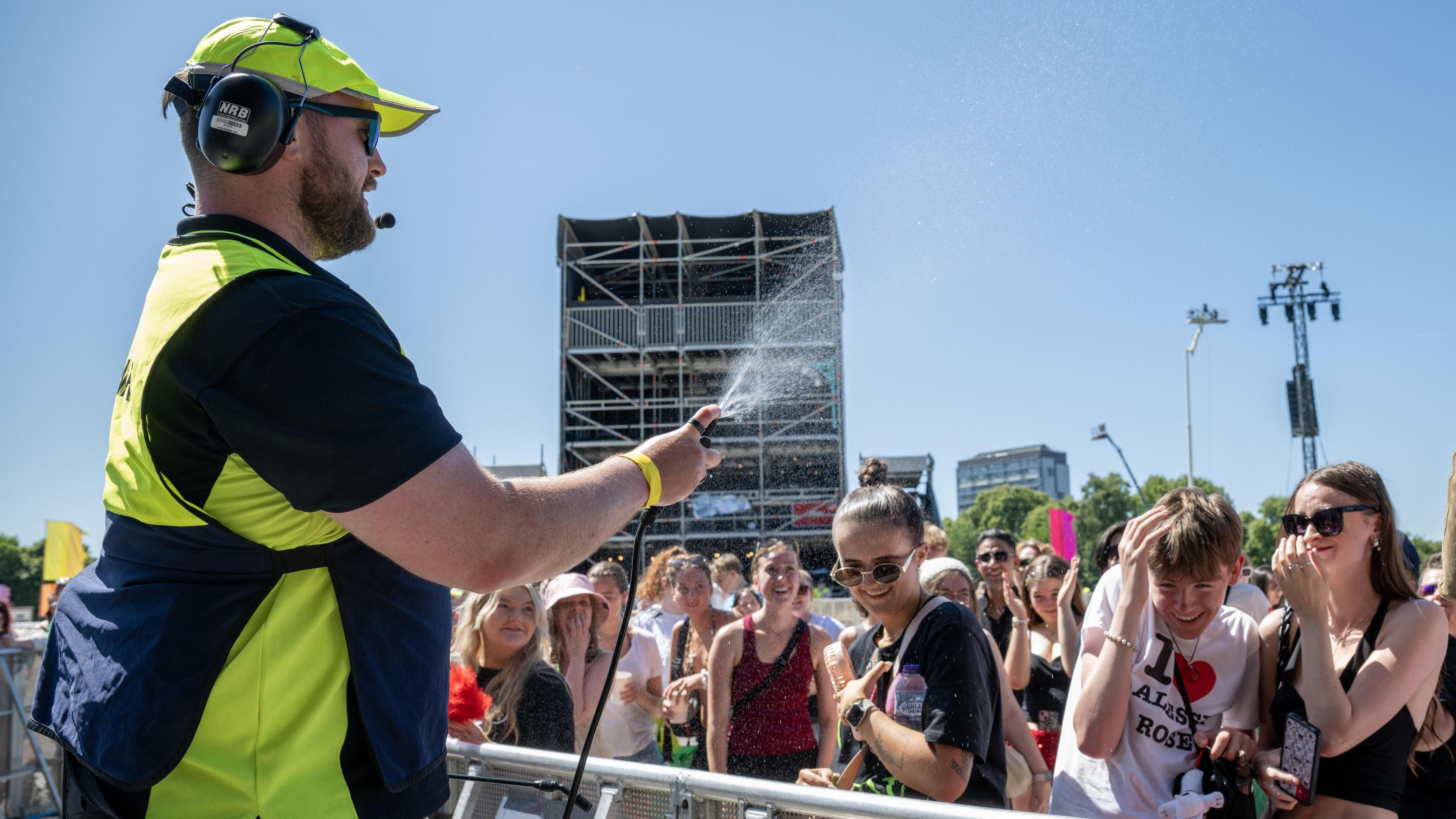A steward sprays water over music fans on a sunny day at TRNSMT