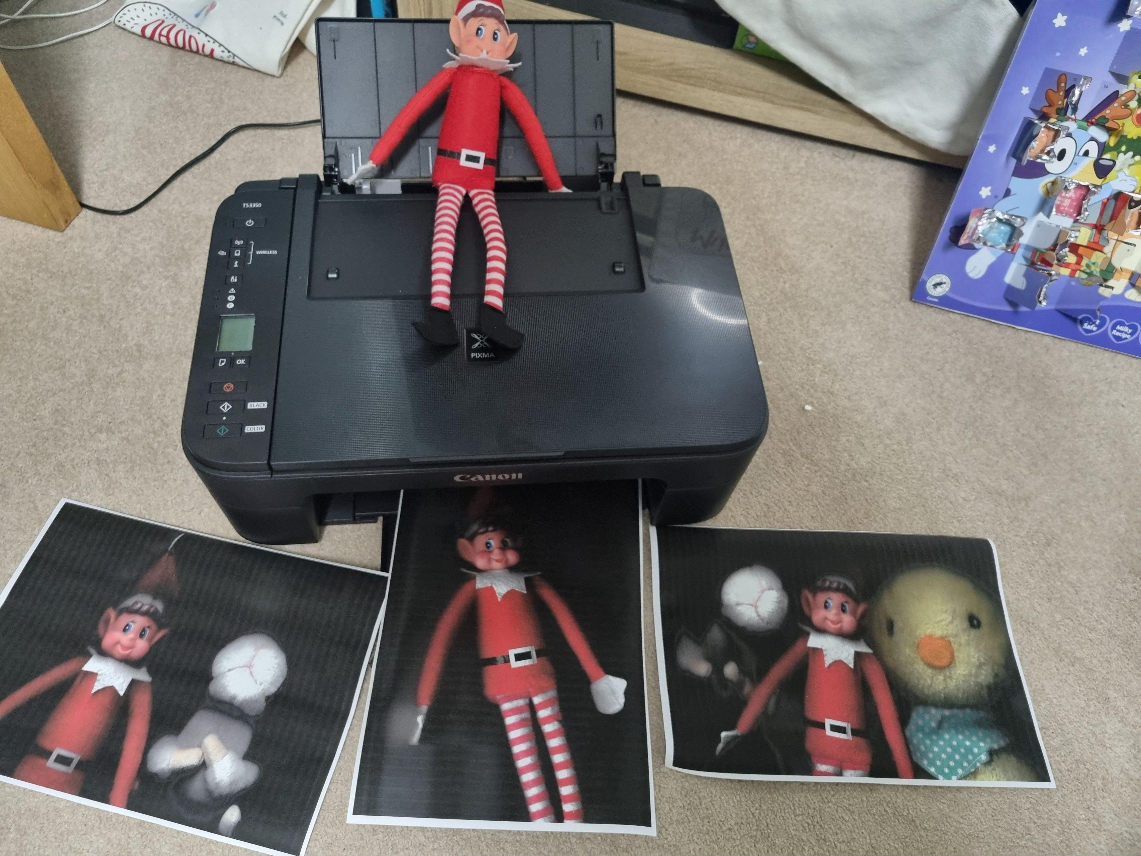 Elf on top of scanner with several print outs. 