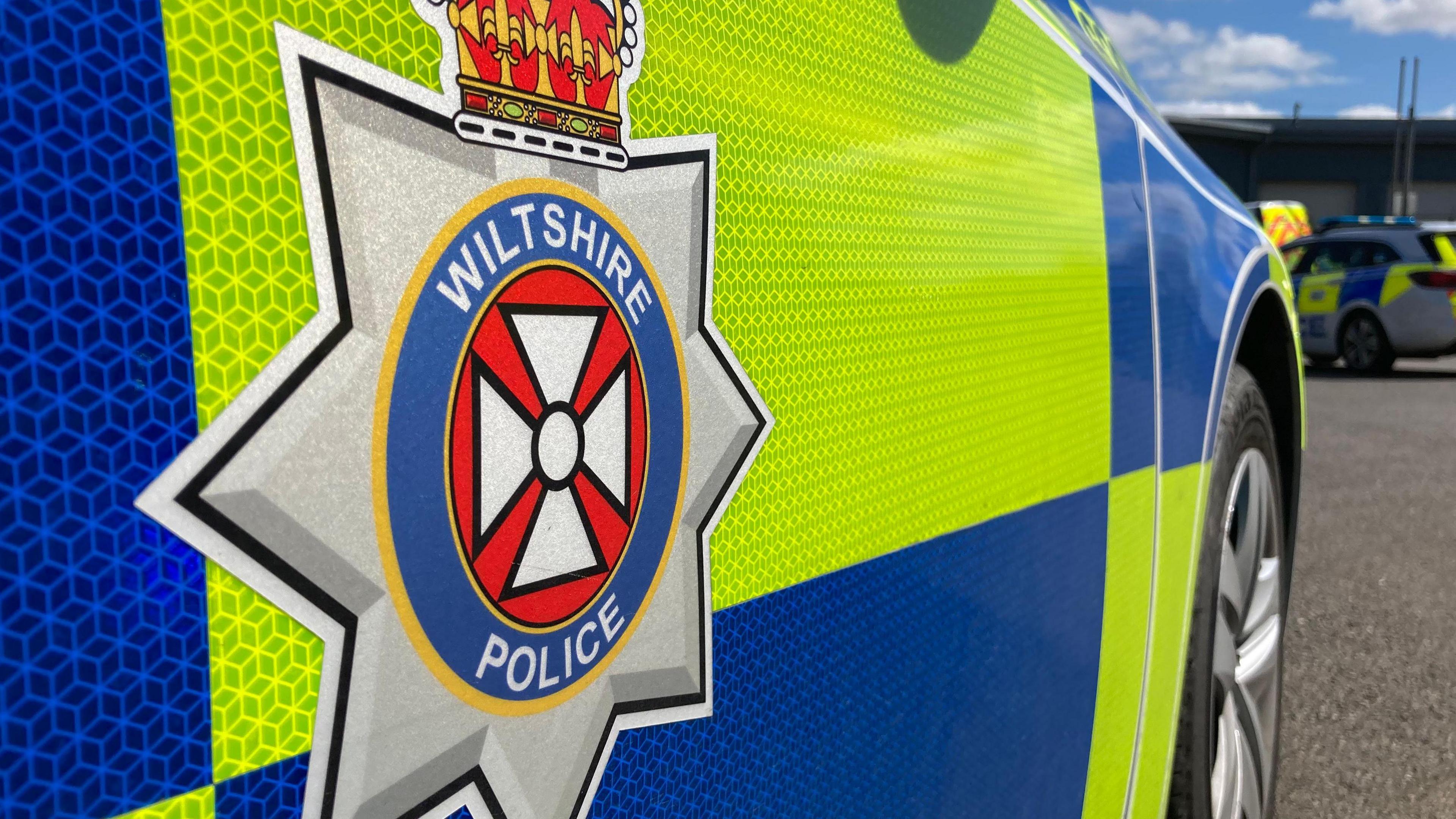 The side of a marked Wiltshire Police car, which has the force's logo on. It is a close up of the driver's side door.