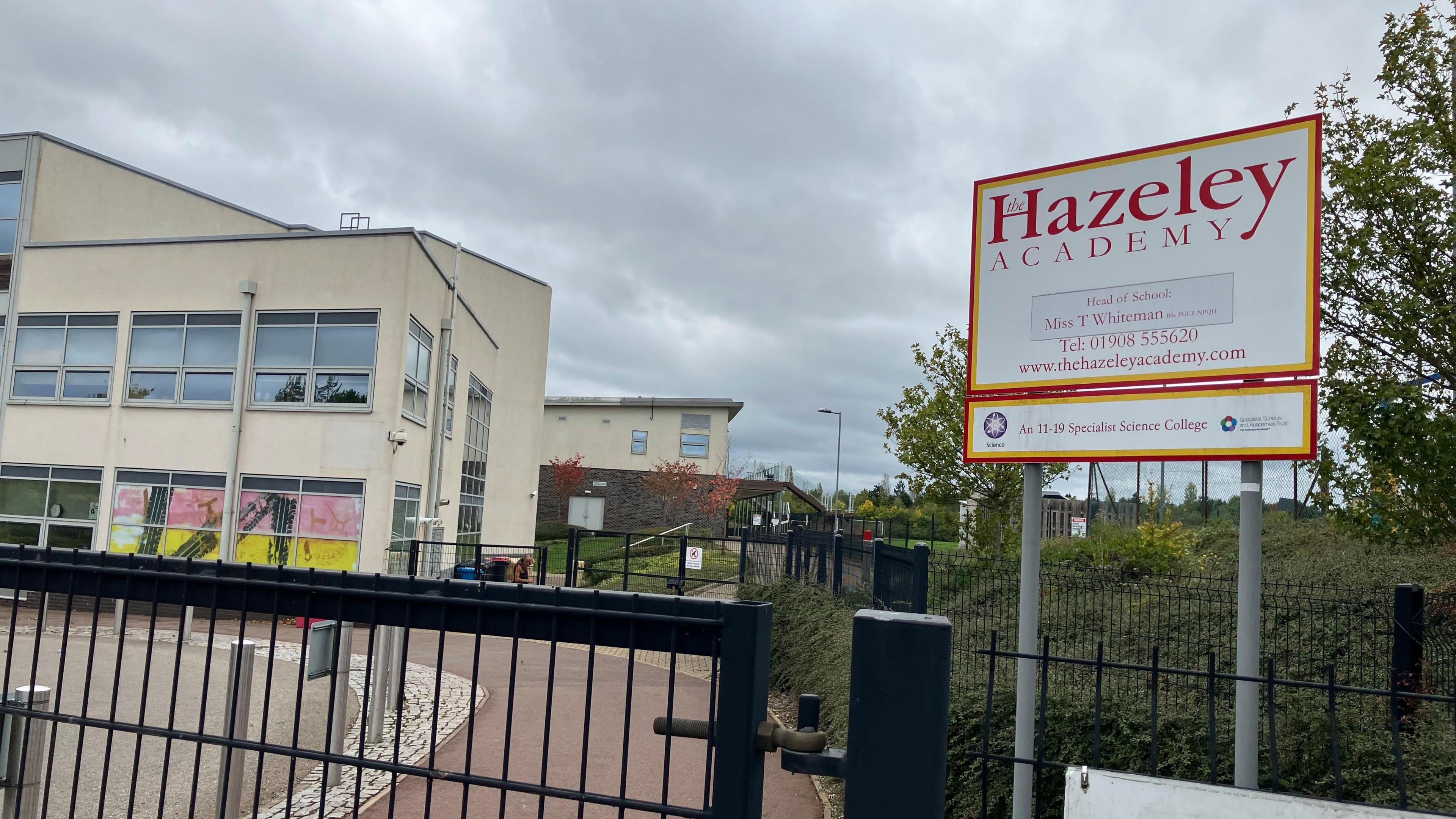 The school gates outside Hazeley Academy where there is a large white sign with the name of the school