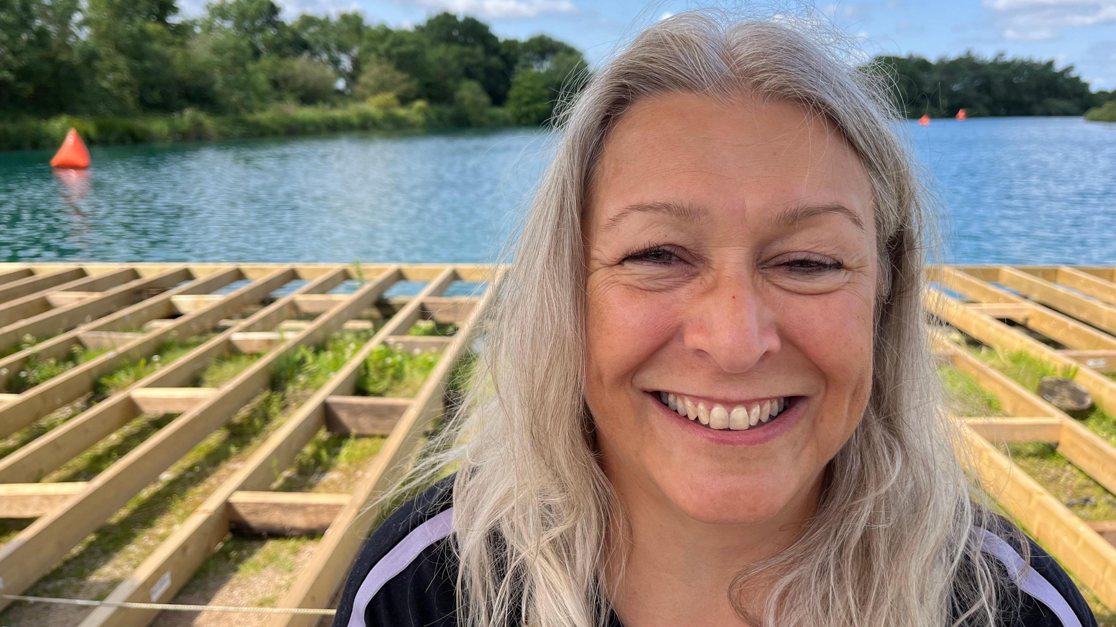 Fiona smiles at the camera with a lake behind her