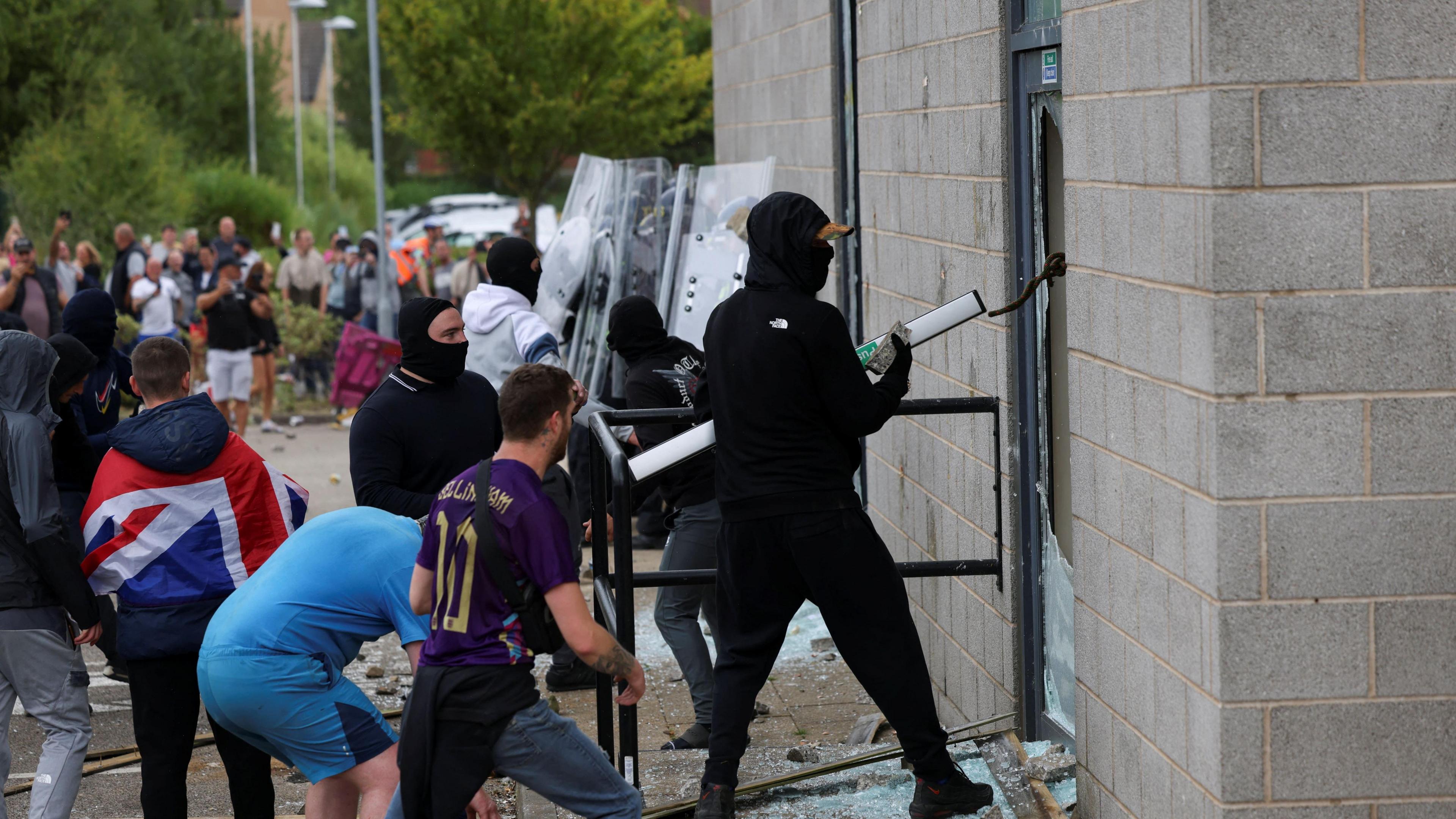 Far-right demonstrators smash windows at The Holiday Inn Express in Rotherham during demonstration. A man dressed in all black with his face covered is at the front.