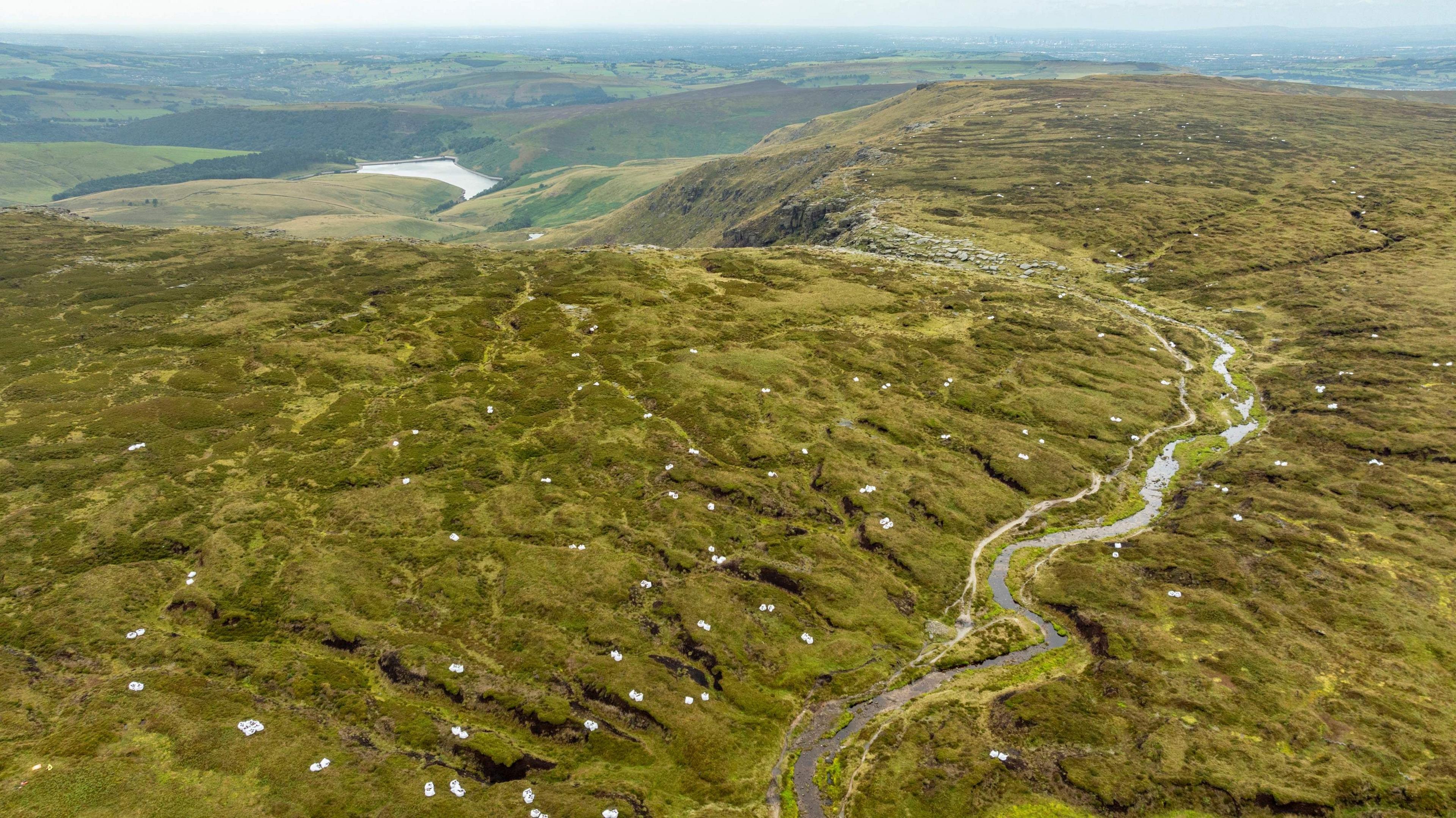 An aerial shot of white bags dotted around the moorland landscape with a reservoir in the distance