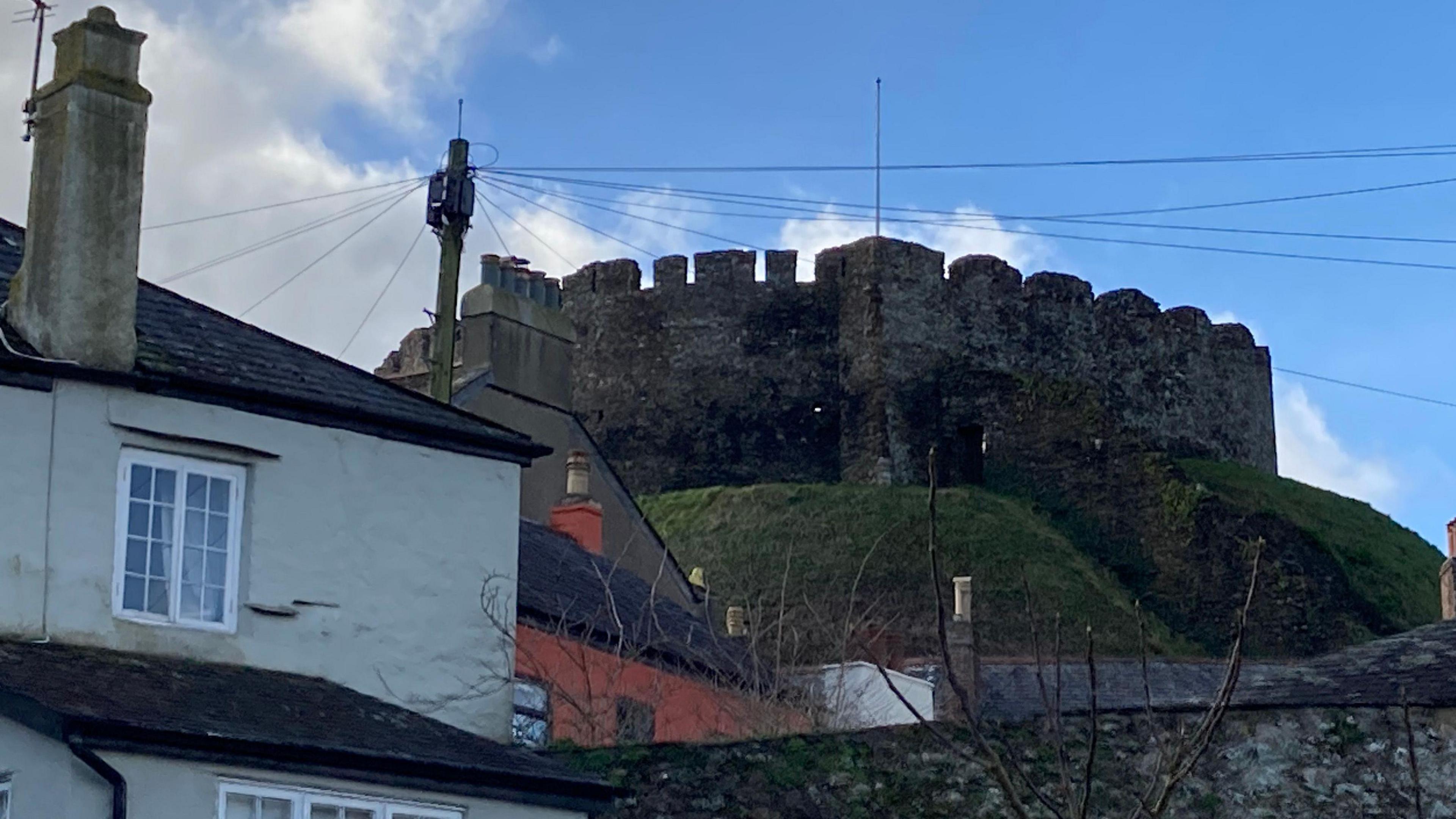 A crenelated tower at the top of of the motte, or mound at Totnes Castle. The roofs of houses can be see in the foreground.