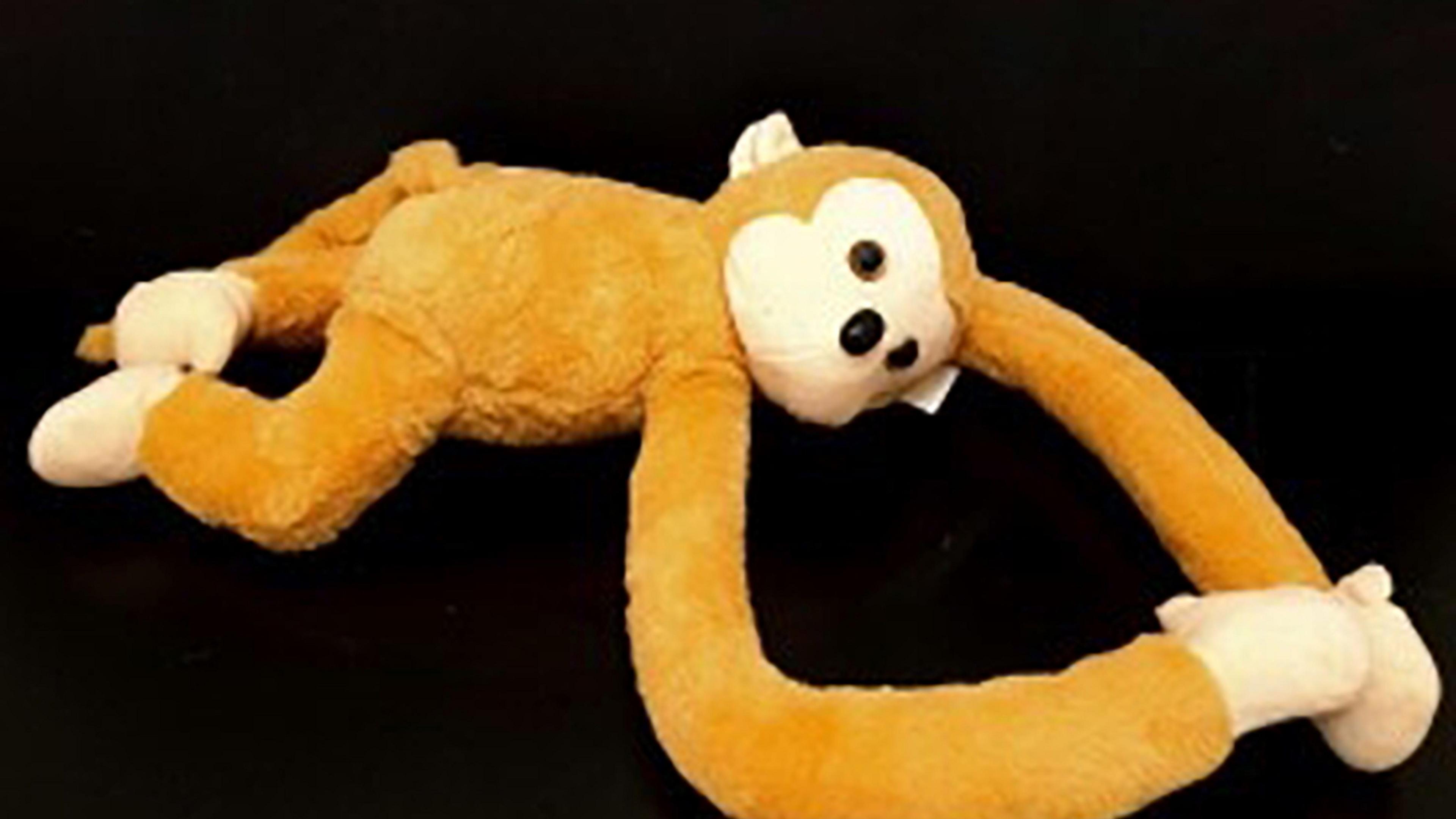 An orange coloured monkey on a black background. It has long front arms that are attached at the hands by a magnet. 