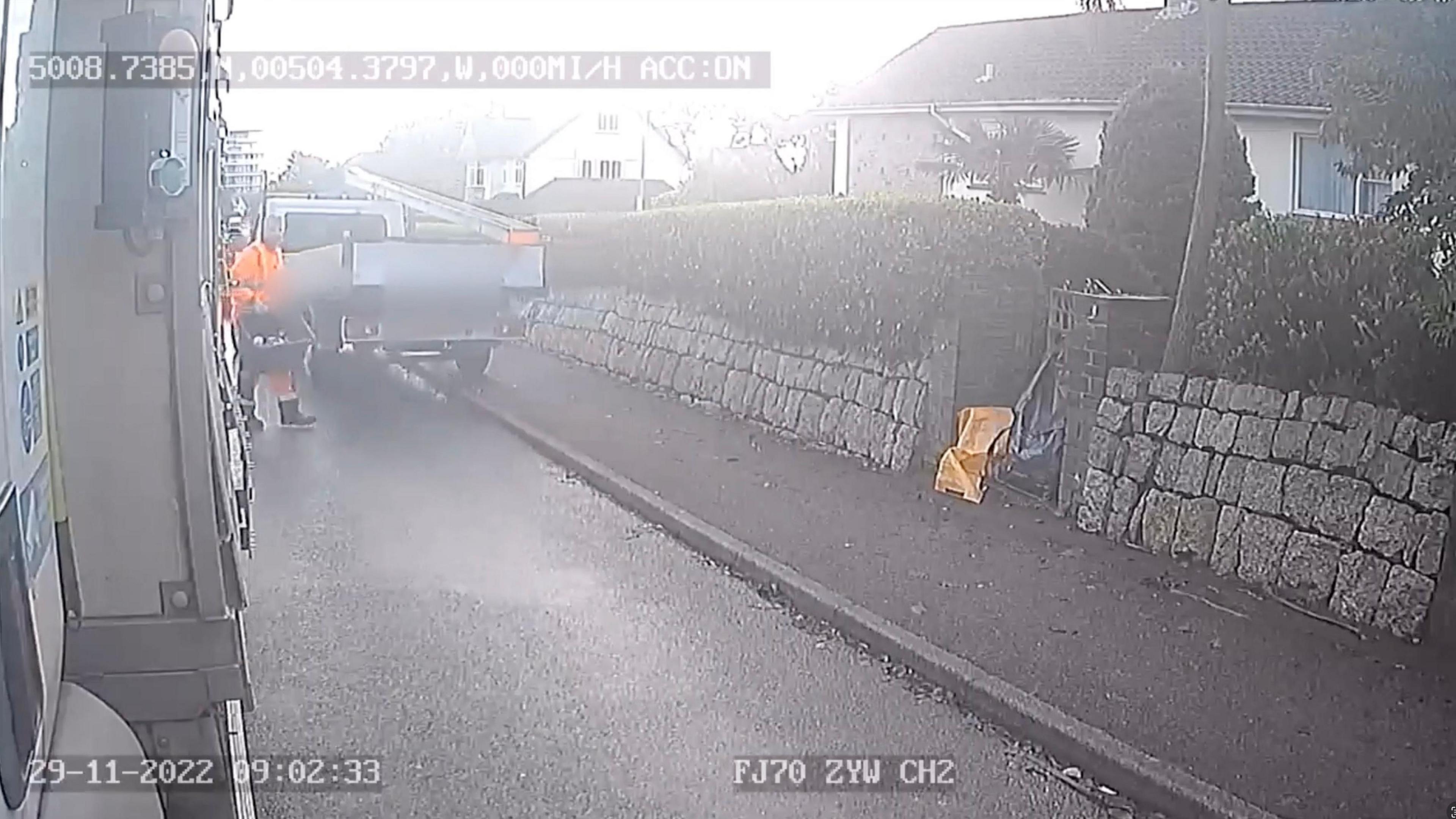 A white van mounts a pavement to get past a bin collection lorry, narrowly missing one of the crew who is wearing brigh orange reflective clothing.