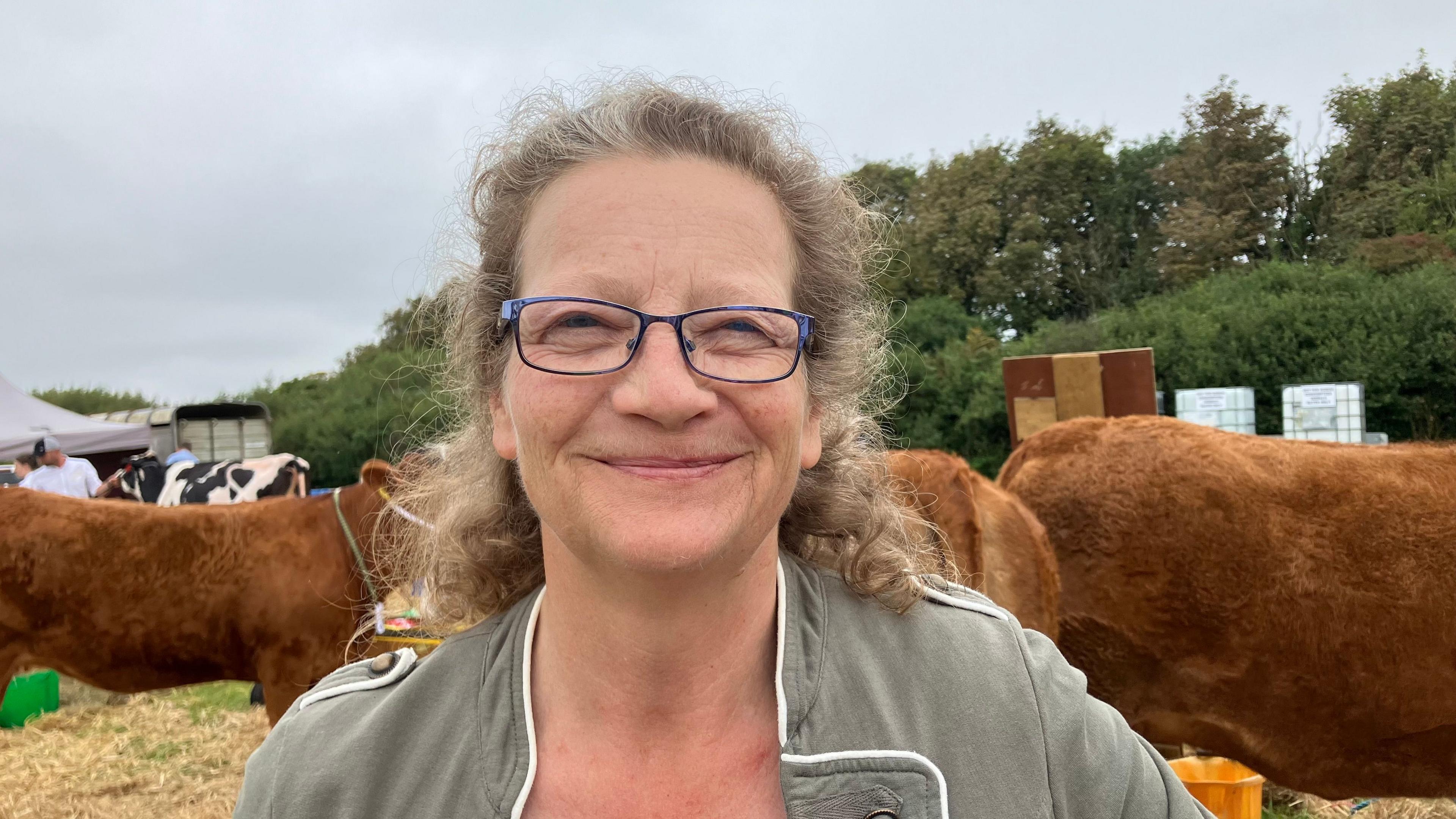 A smiling woman wearing glasses in front of some brown cows.